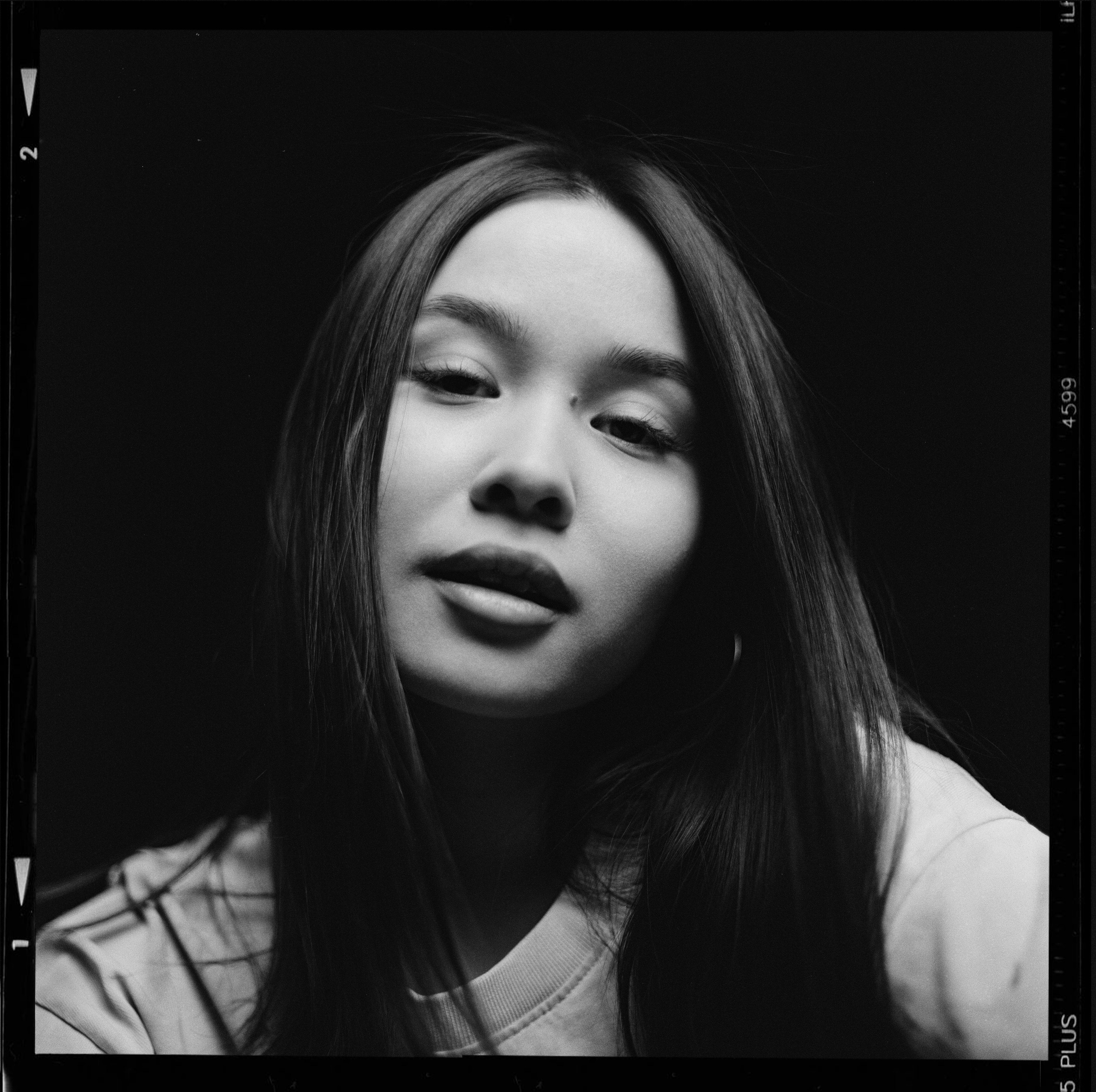 Красивая девушка азиатской внешности на черном фоне смотрит в камеру