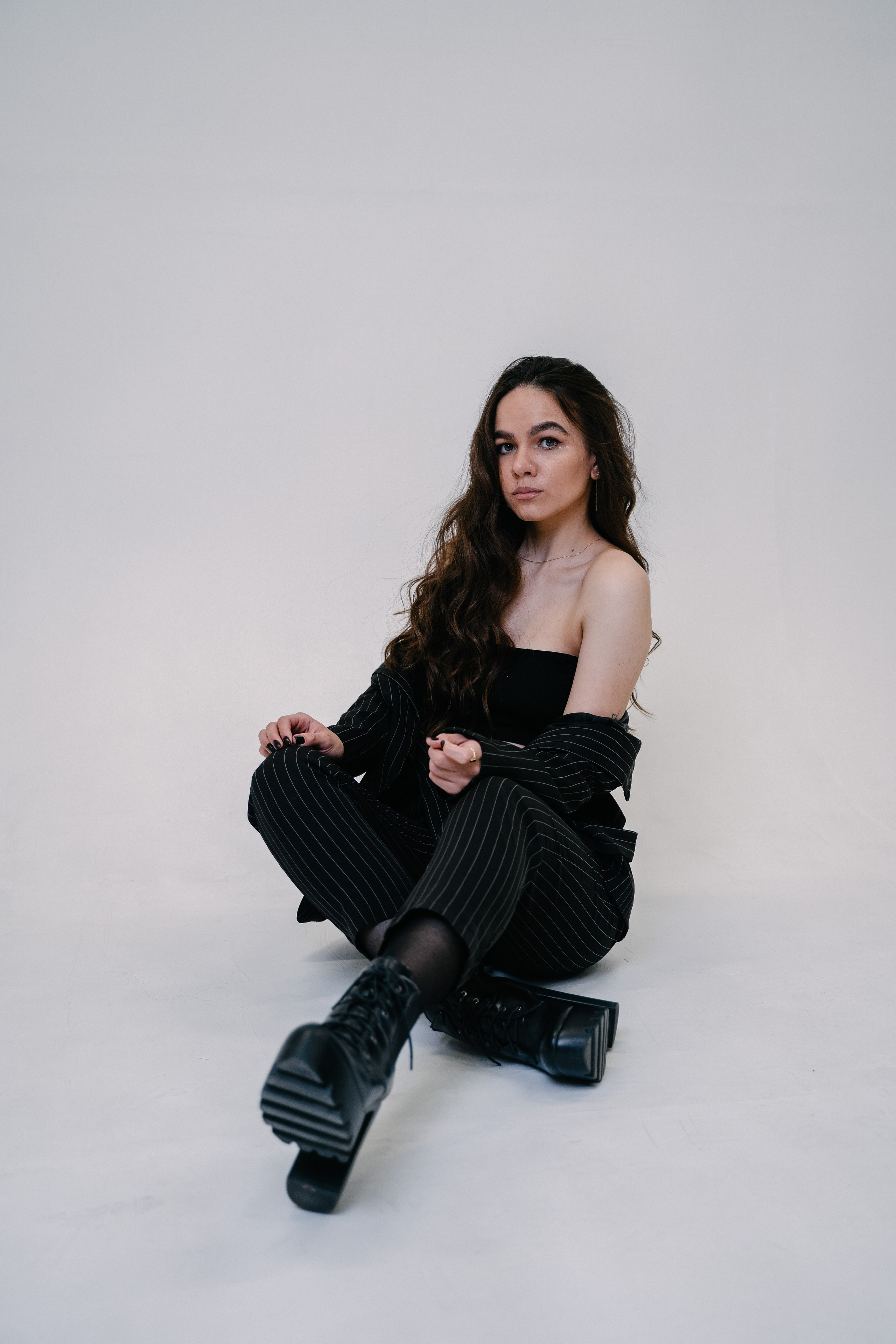 девушка сидит на белом фоне в черном костюме