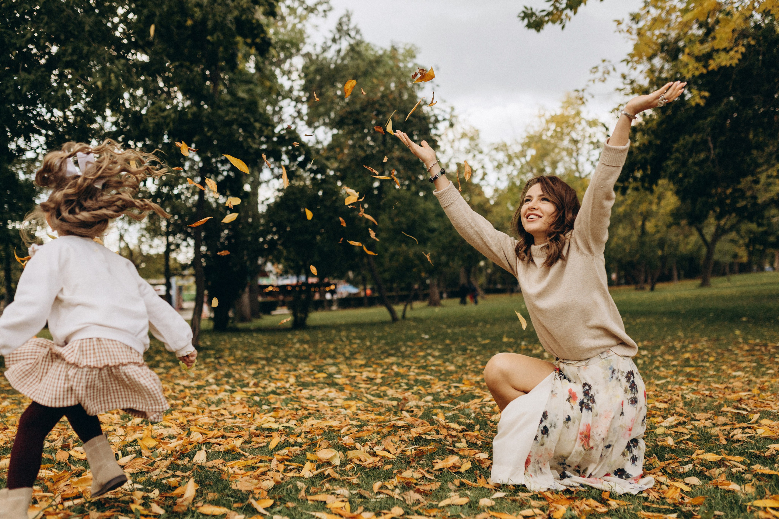 мама и дочка играют с листвой в парке