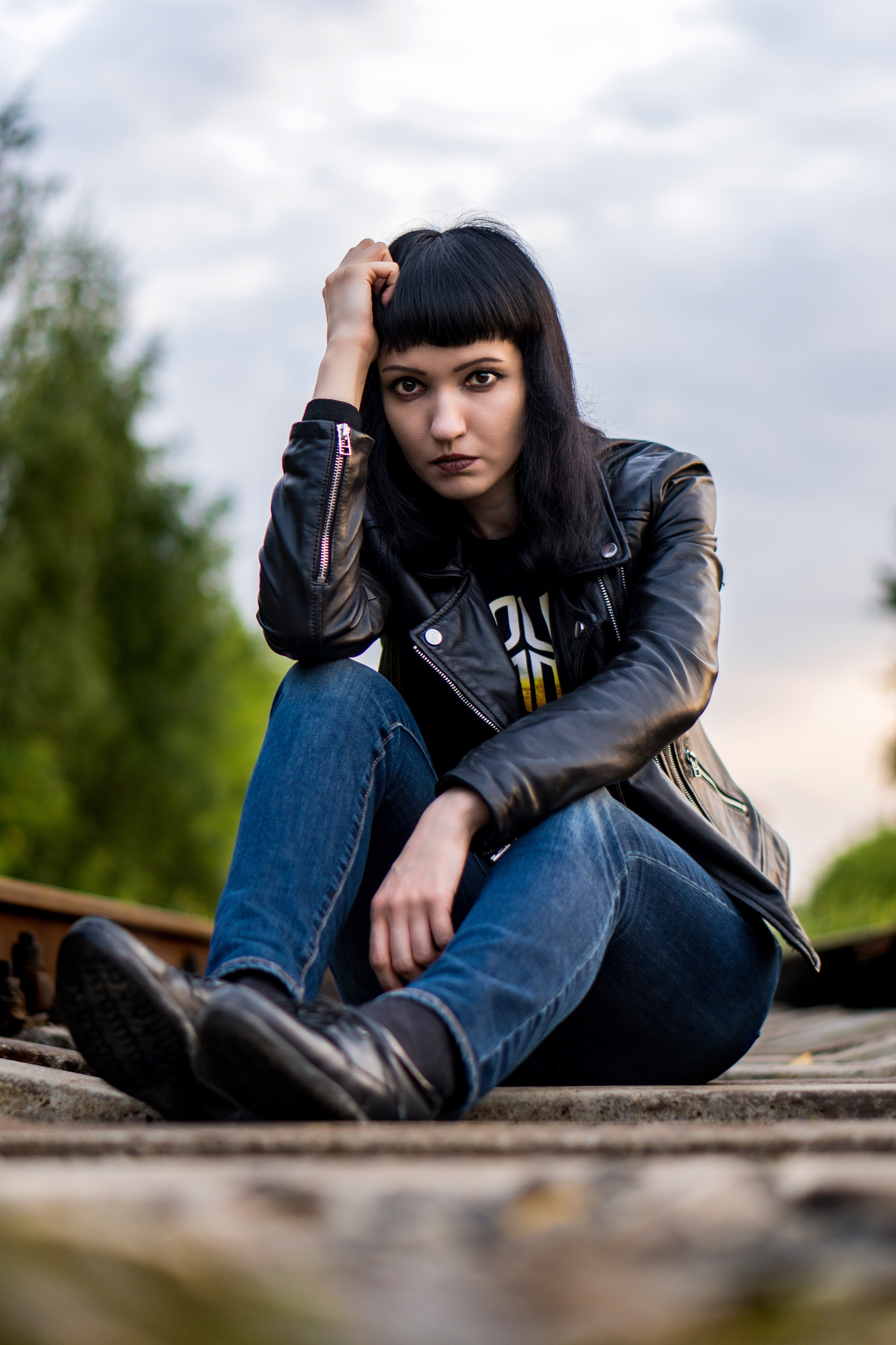 железная дорога. на путях сидит девушка в черной кожаной куртке и джинсах