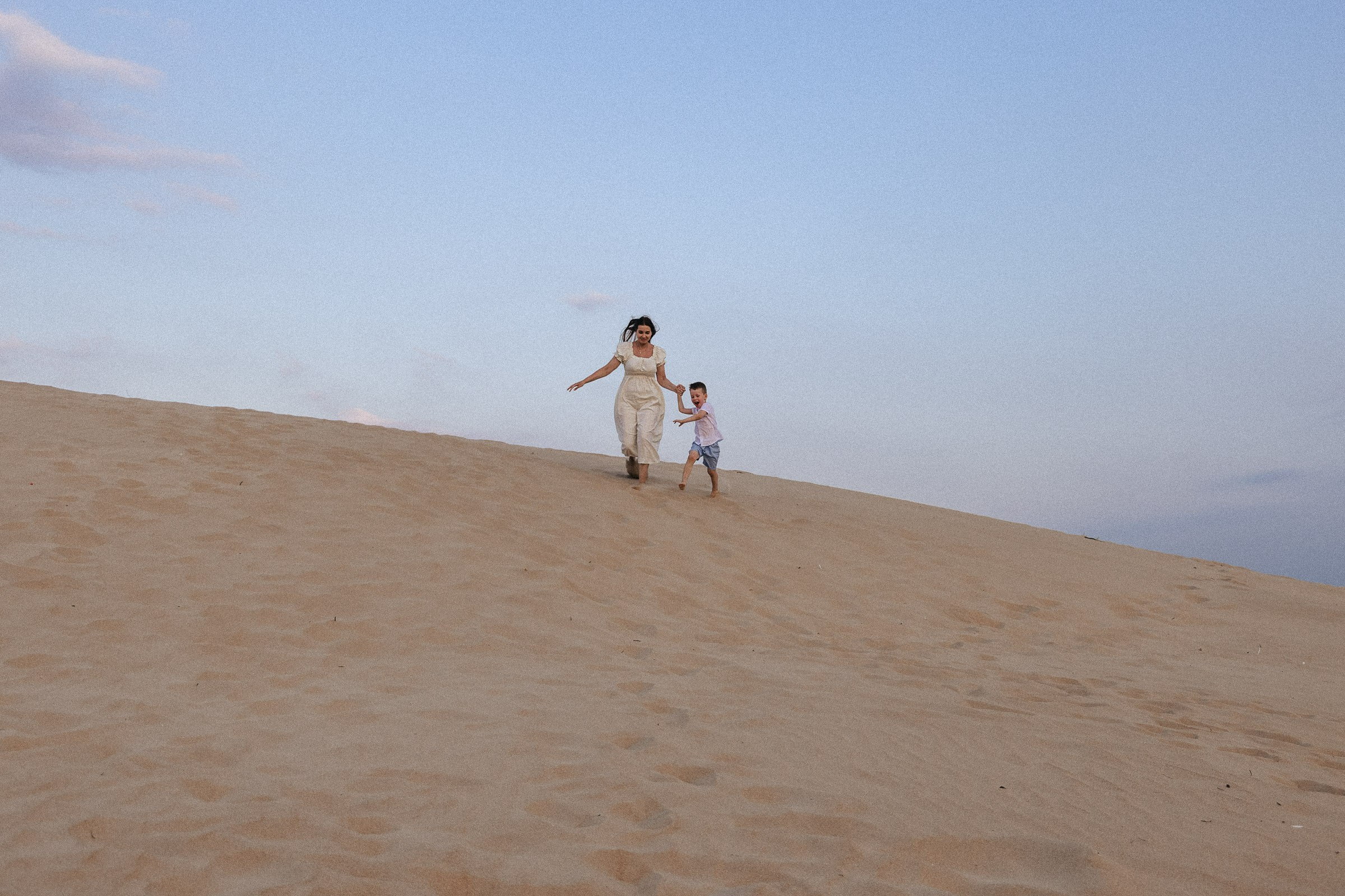 мама и сын бегут с песчаной дюны вниз