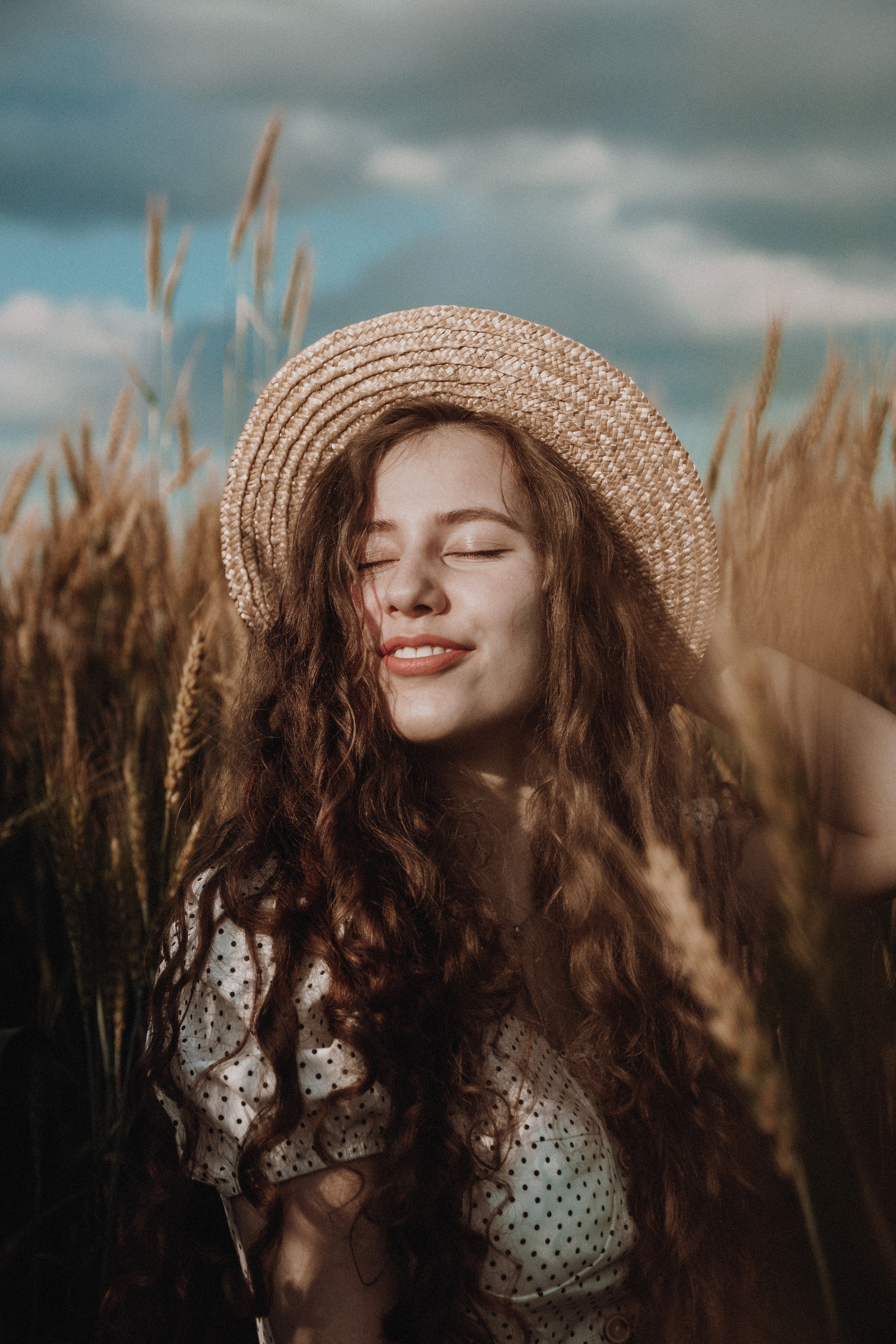 Девушка в шляпе улыбается сидя в поле ржи