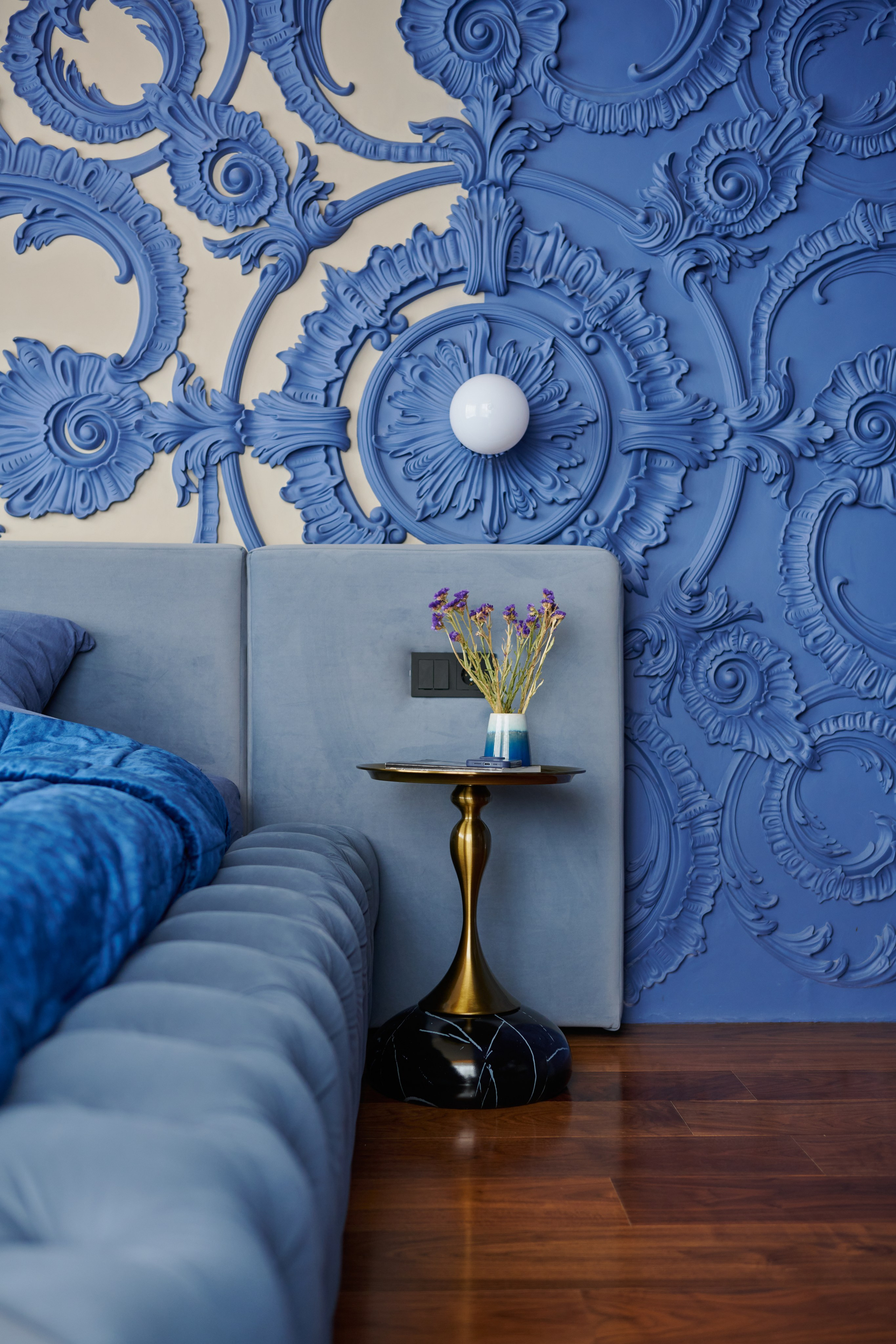 Спальня с синей лепниной, серым изголовьем и бра