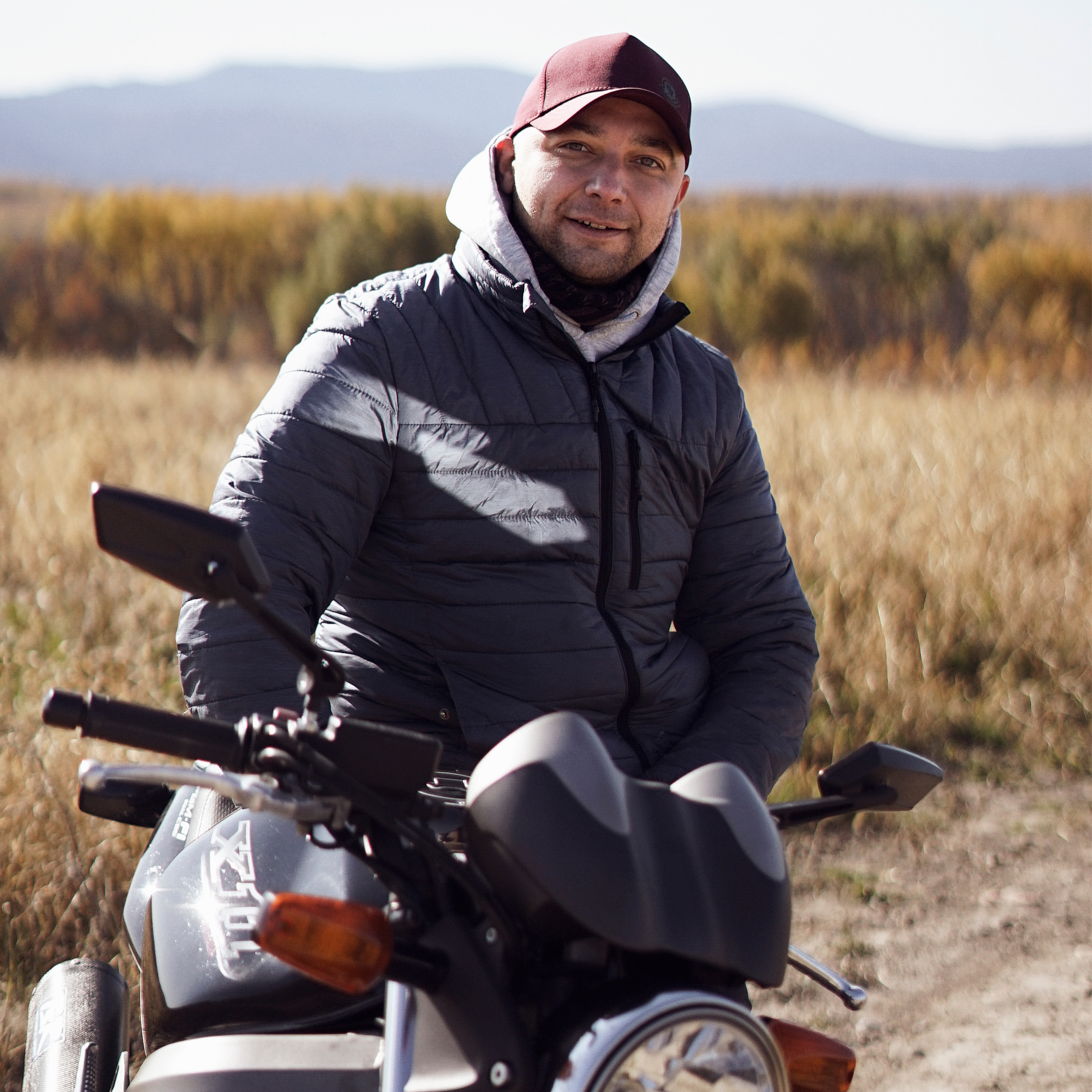 Портрет мужчины с мотоциклом на фоне поля и гор