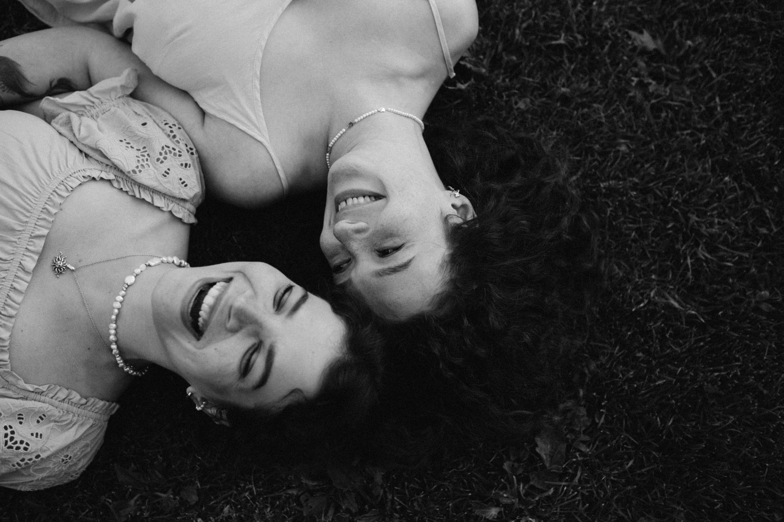 Две подружки лежат рядом на поляне и смеются