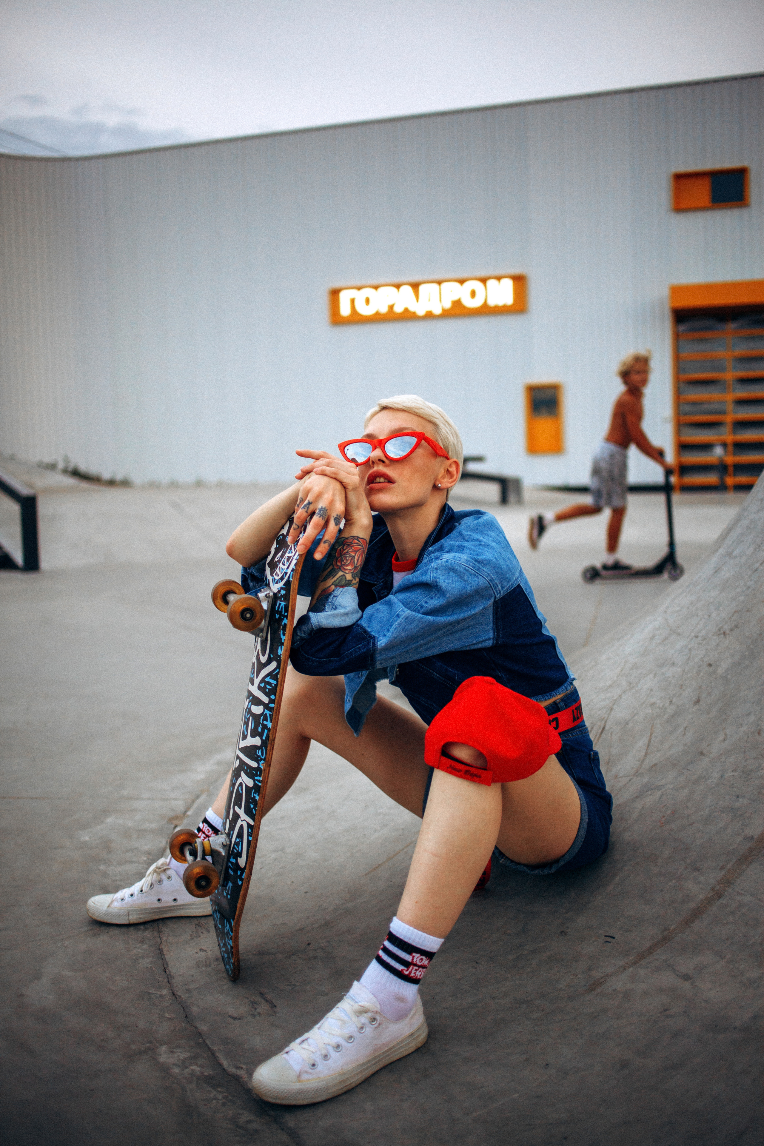 Девушка в красной кепке сидит в скейт=парке на закате