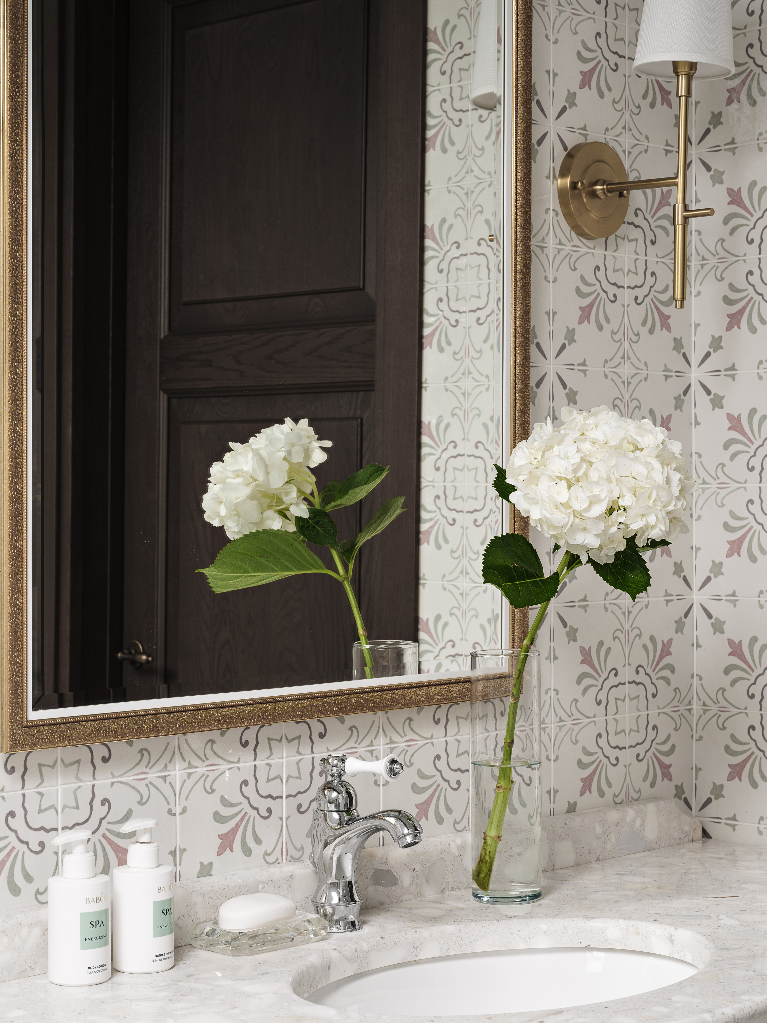 Декор ванной комнаты с раковиной на каменной столешнице, настенной плиткой с орнаментом, бронзовым зеркалом и букетом белых гортензий в стеклянной вазе; работа дизайнера Валерии Хростовской, съёмка Сергея Денисенко.