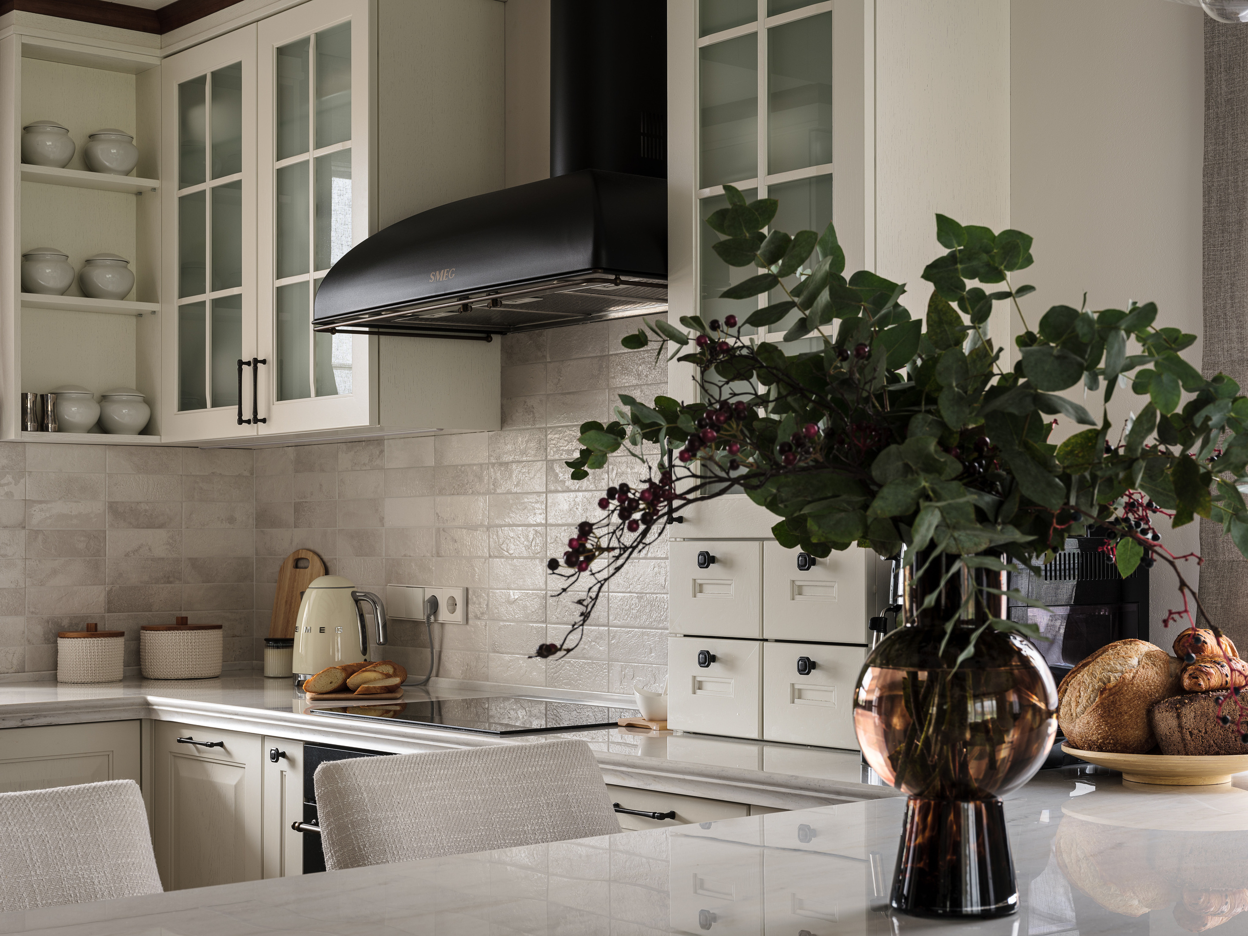 Стильная кухня с барной стойкой, светлыми шкафами с витражными фасадами, черной вытяжкой Smeg и акцентами в бежевых и древесных оттенках. Декор с зеленью в вазе и мягкими креслами у острова. Дизайнер Валерия Хростовская, фото Сергей Денисенко.