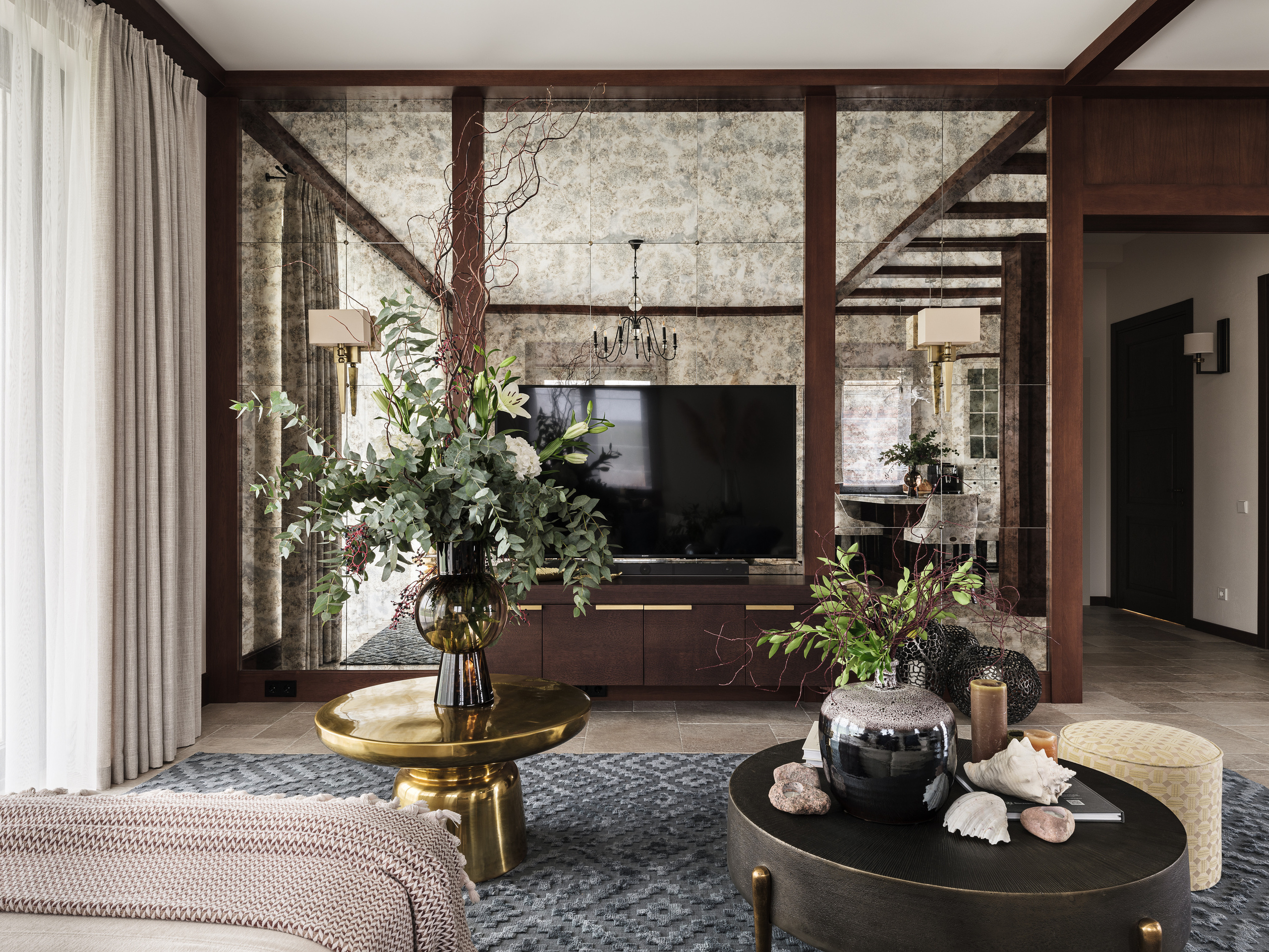 Современная гостиная с телевизором на фоне зеркальной стены, золотистым и темным журнальными столиками с декором, вазами и живыми цветами. Контрастная и уютная композиция. Автор интерьера Валерия Хростовская, фото Сергей Денисенко.