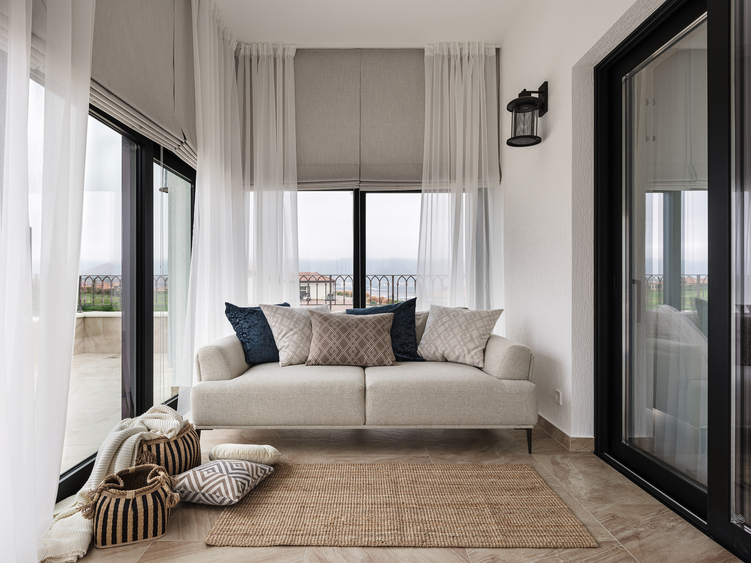 Современная светлая гостиная с бежевым диваном, декоративными подушками, корзинами и текстилем в скандинавском стиле у панорамных окон; дизайн интерьера Валерии Хростовской, интерьерная стилизация и фото Сергея Денисенко.