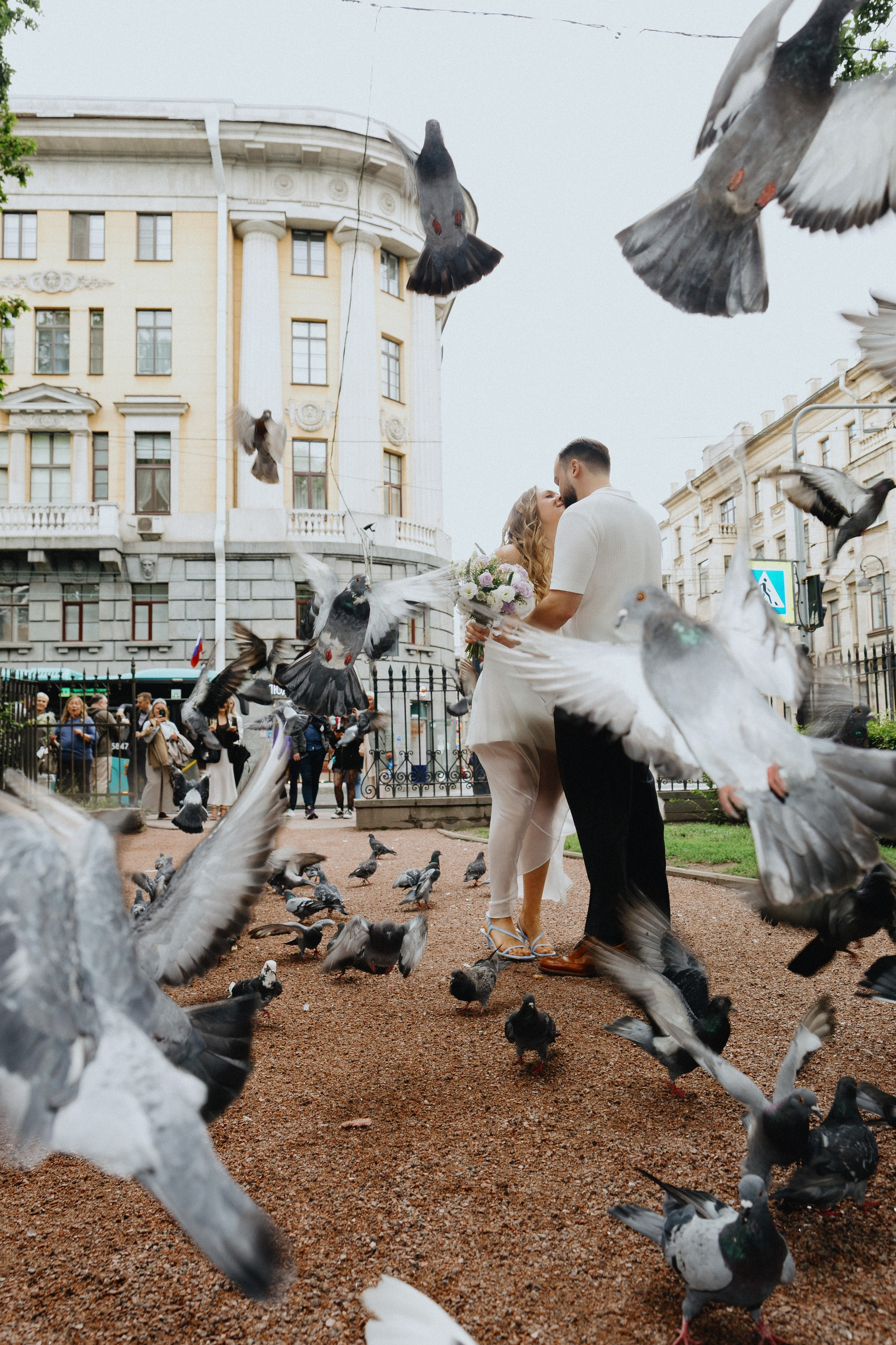 Свадебная фотосессия с голубями: жених и невеста среди стаи птиц в парке.