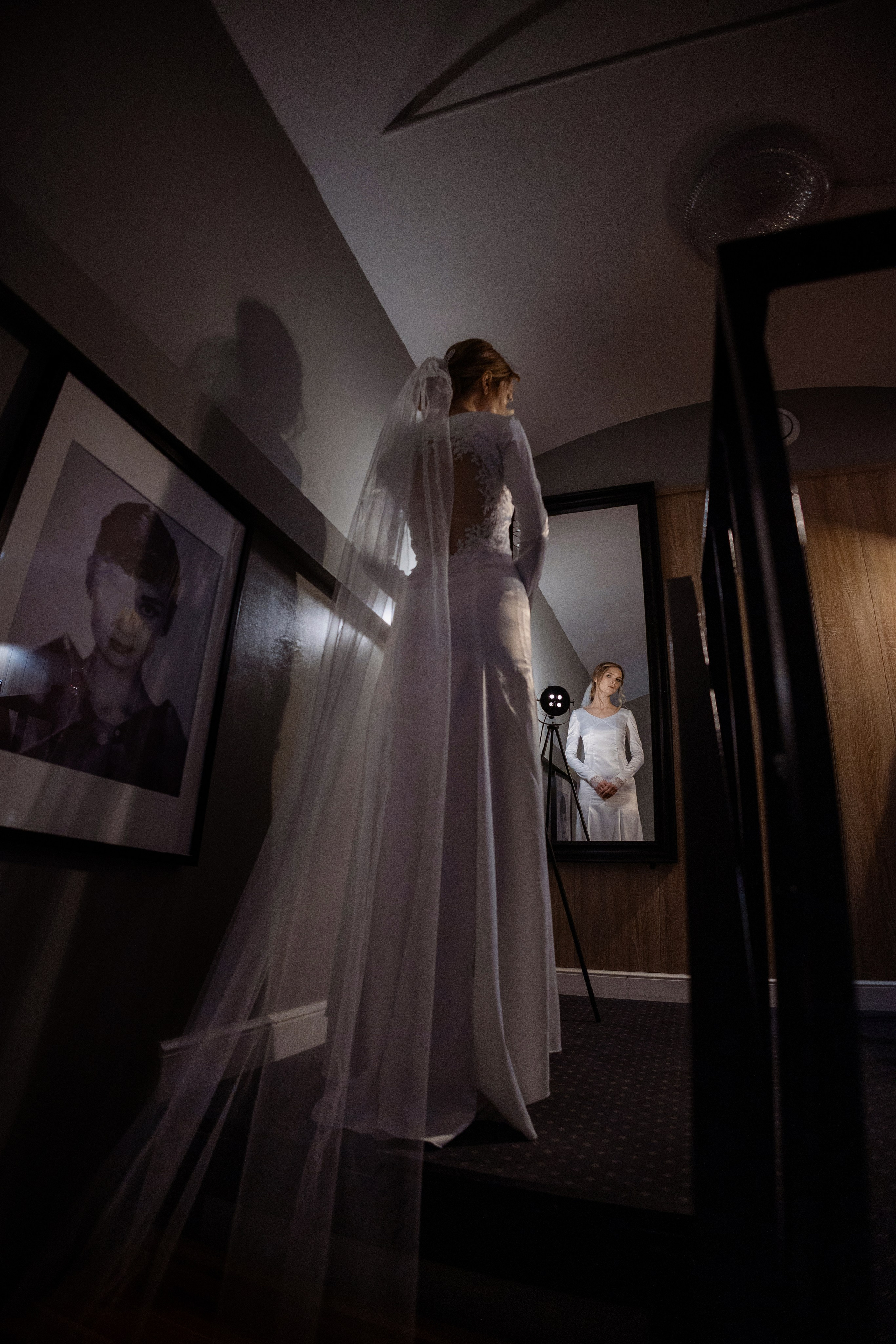Невеста в полумраке стоит спиной у зеркала.