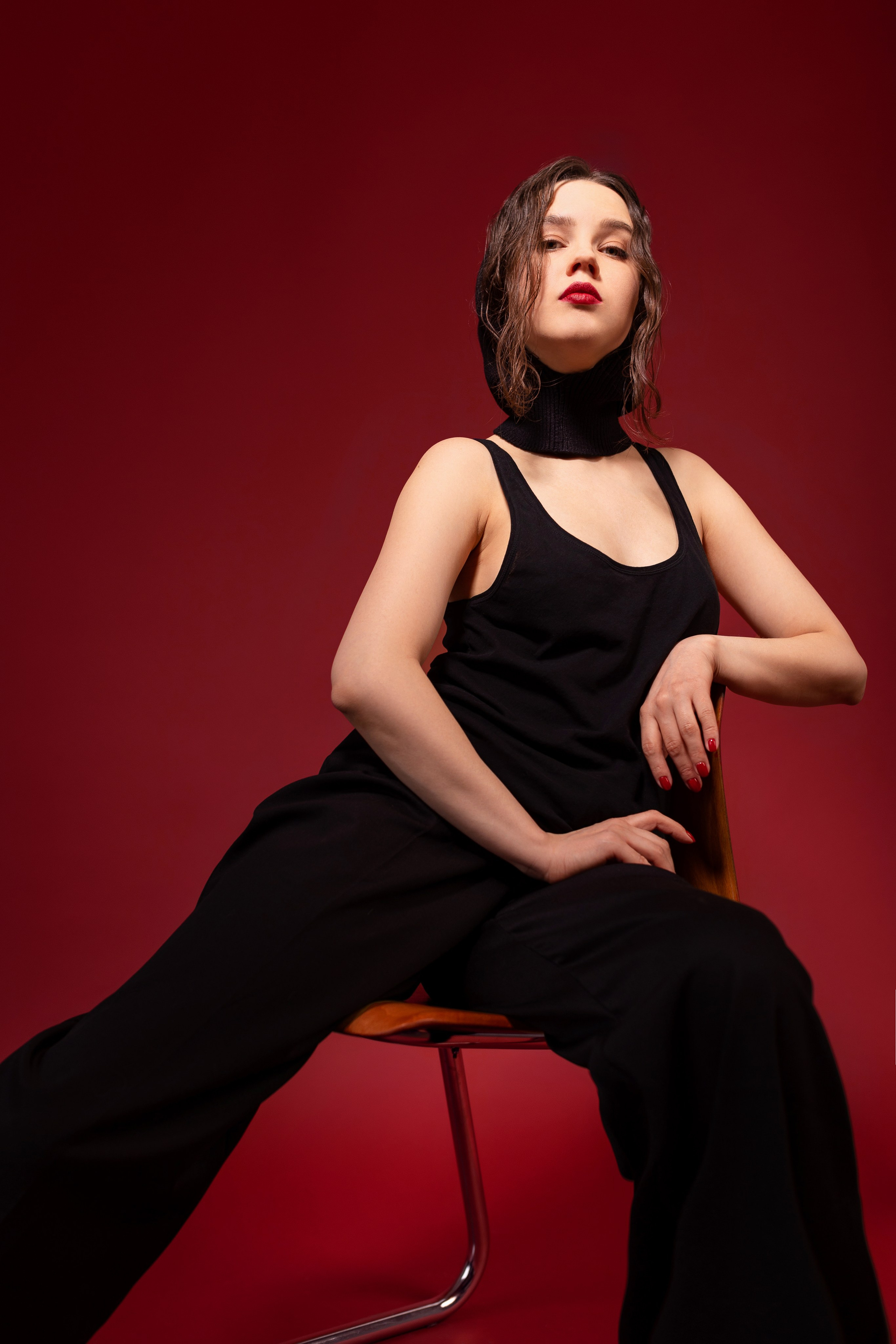 Девушка в стильным чёрном костюме позирует на красном фоне