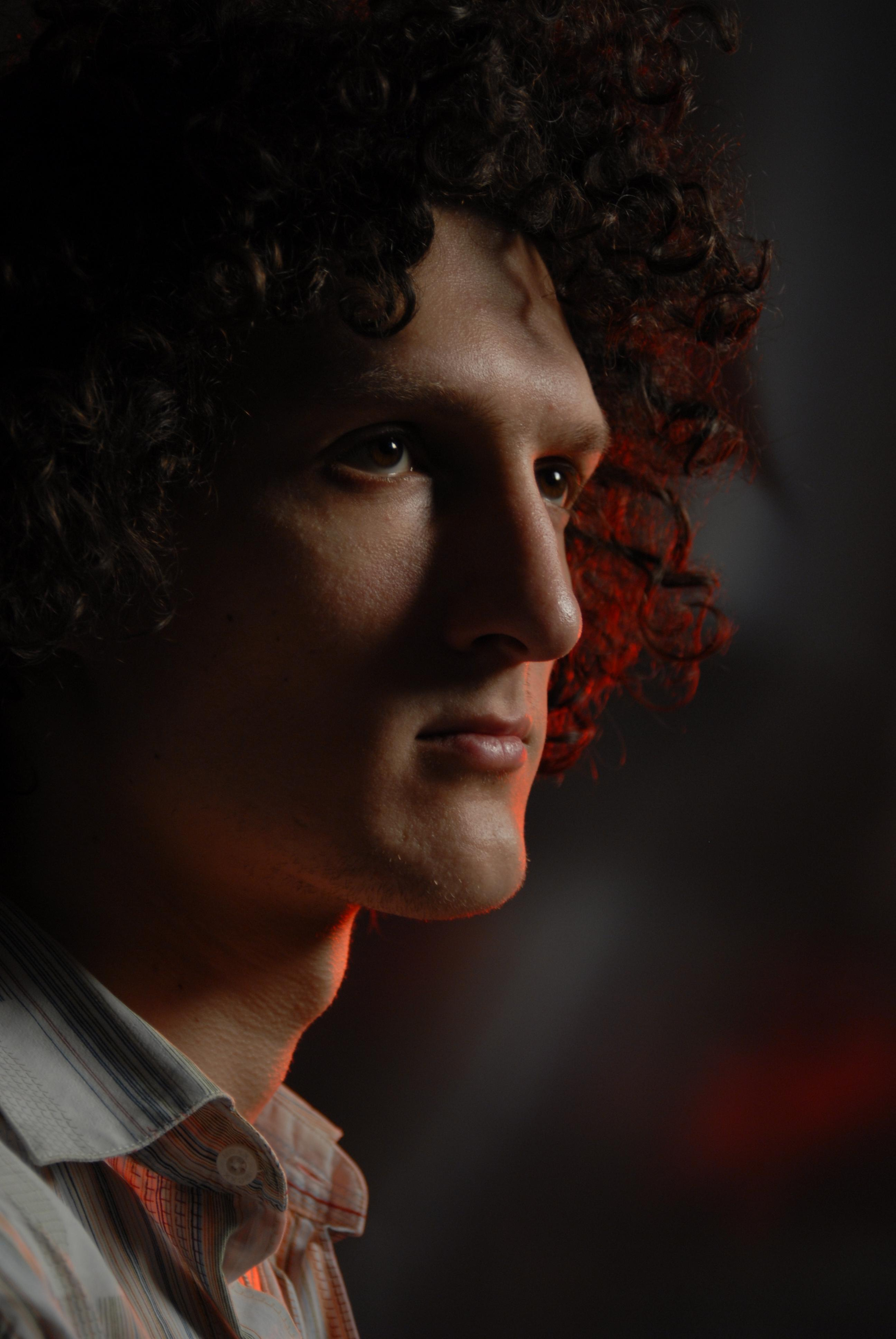 Молодой человек с кудрявыми черными волосами.  Красные световые пятна.