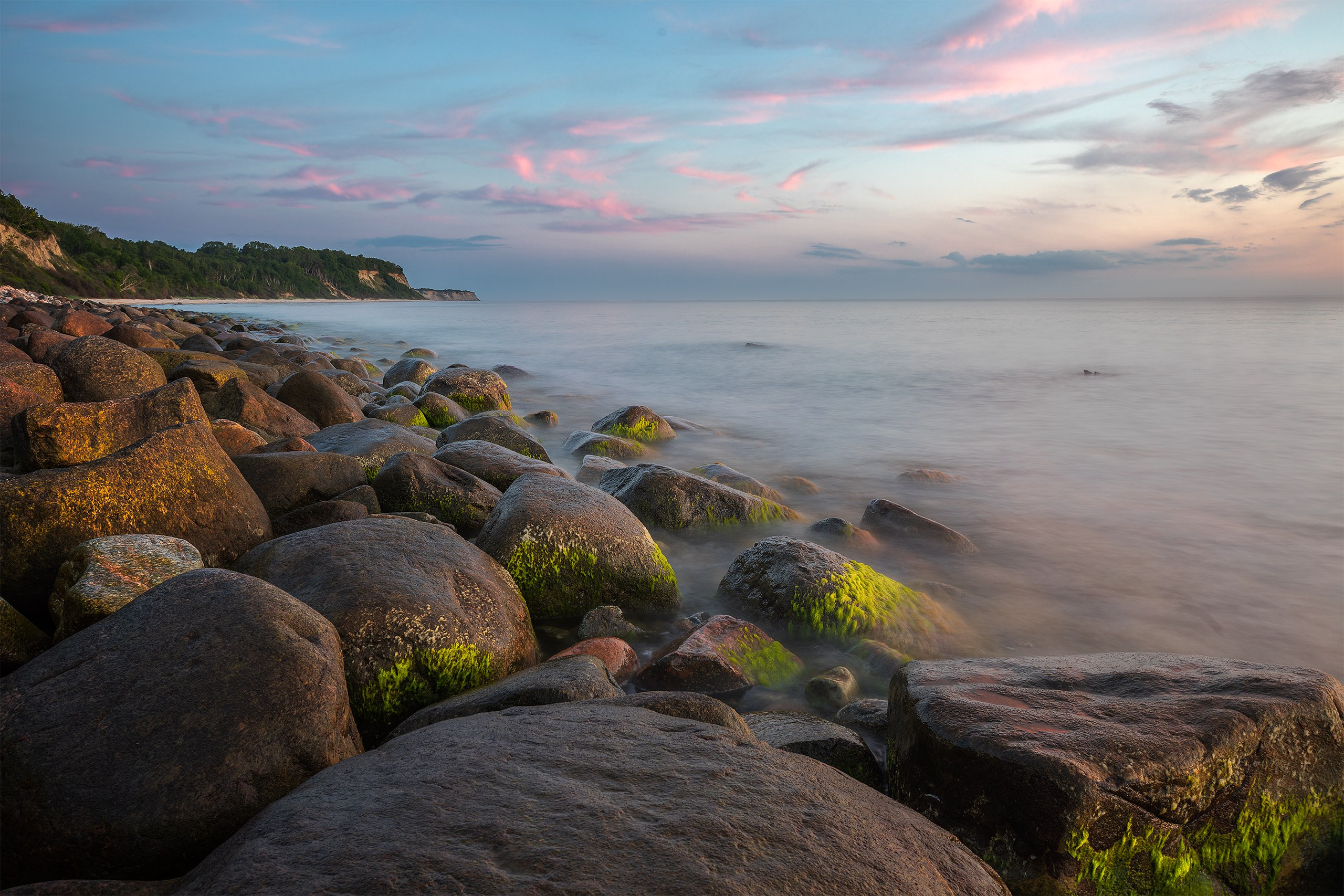 Long exposure seascape photography at Brüsterort with misty smooth water flowing around algae-covered stones under a dramatic evening sky.