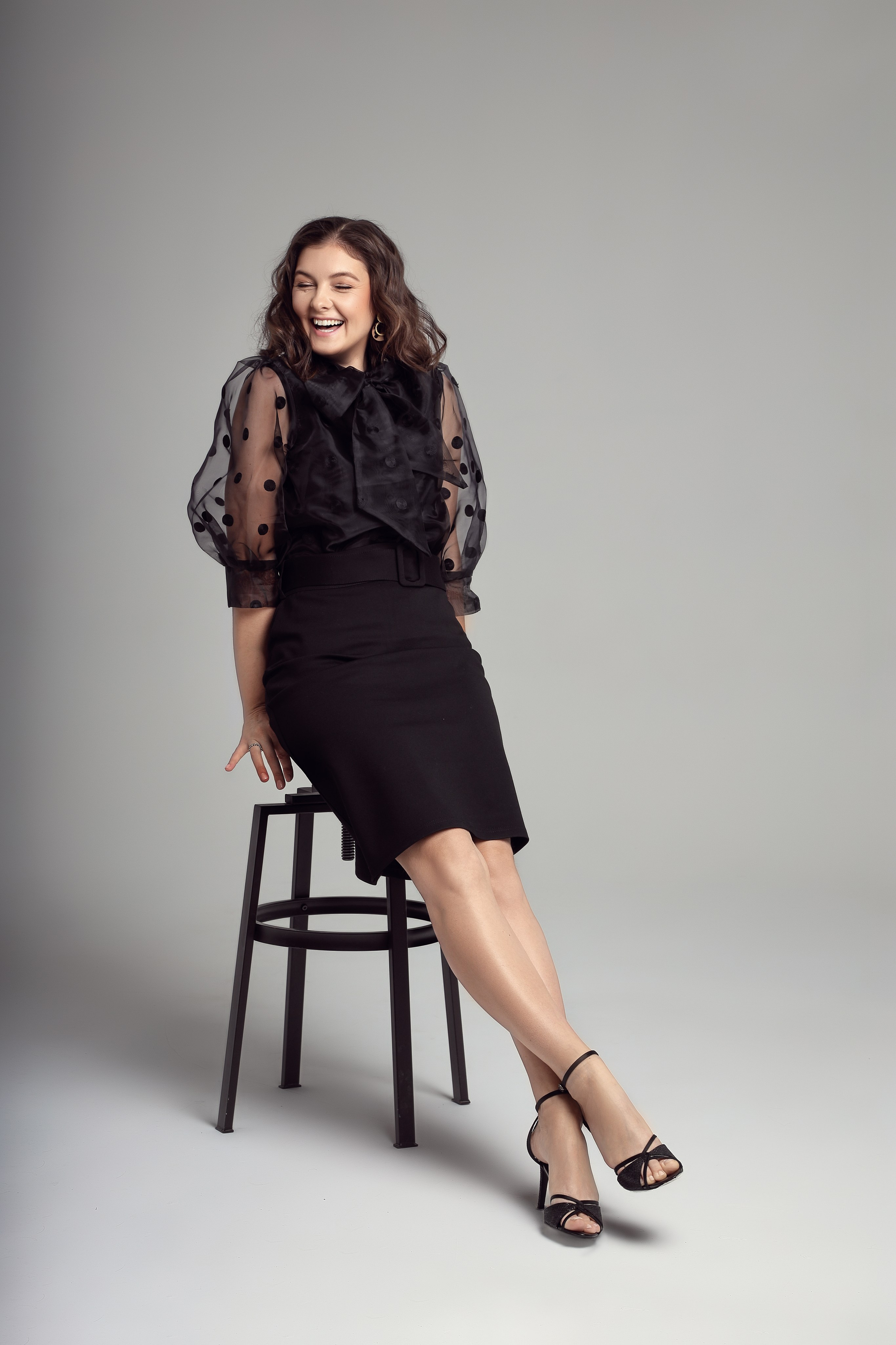 Девушка на стуле в студии смеётся — женская фотосессия в минималистичном стиле.