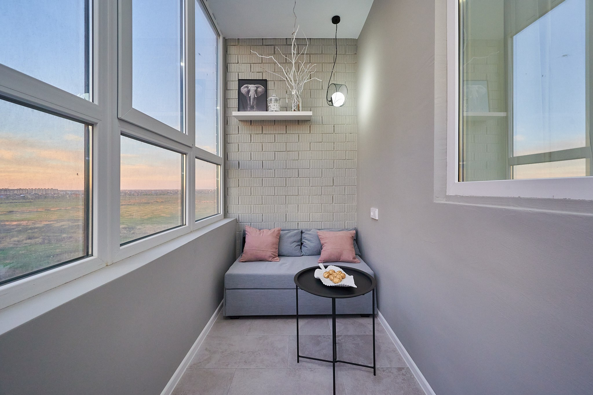 широки балкон в серых цветах с диваном и черным металлическим столиком