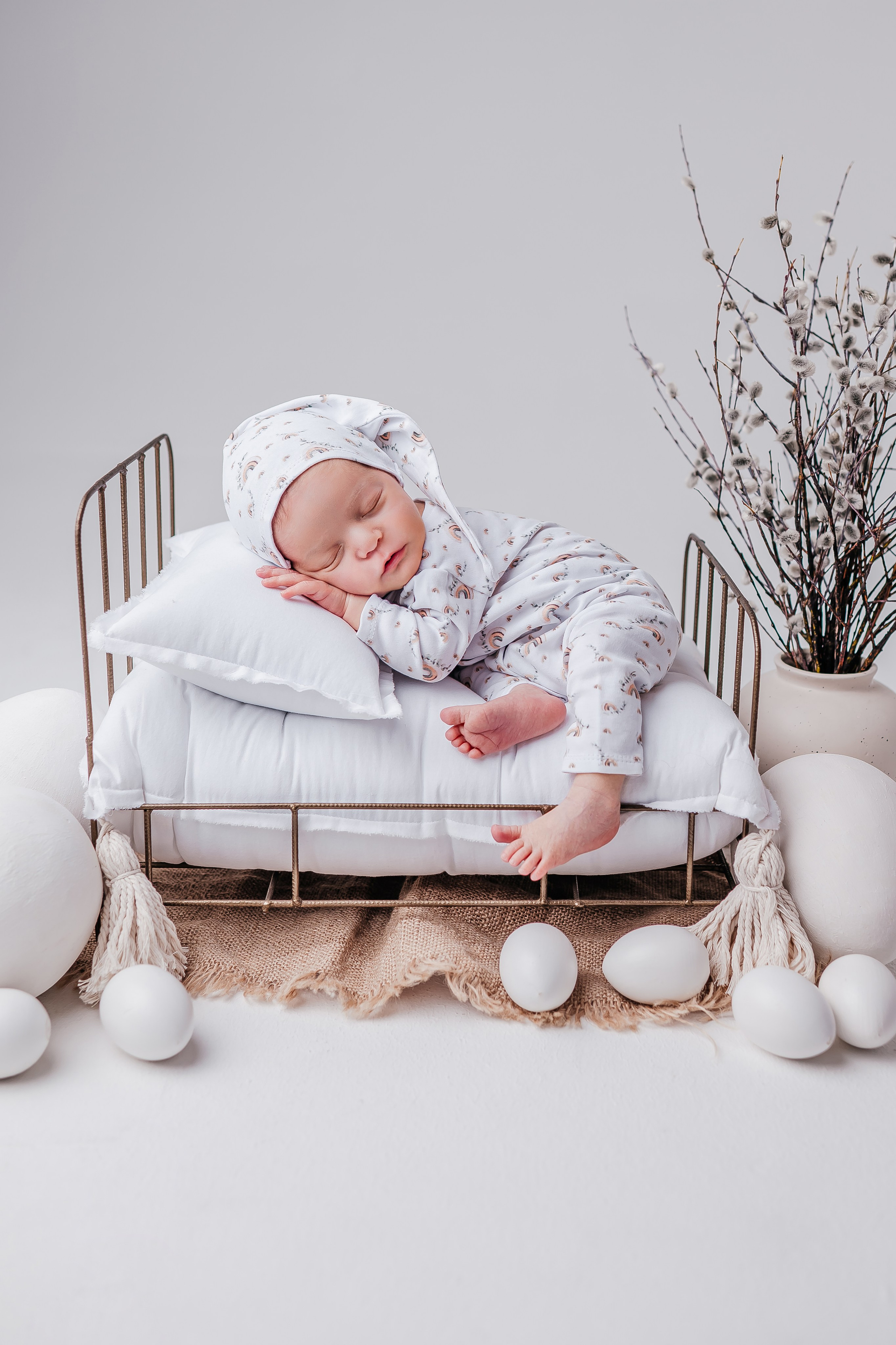 Новорожденный малыш лежит в маленькой кроватке, ножка свисает с кровати