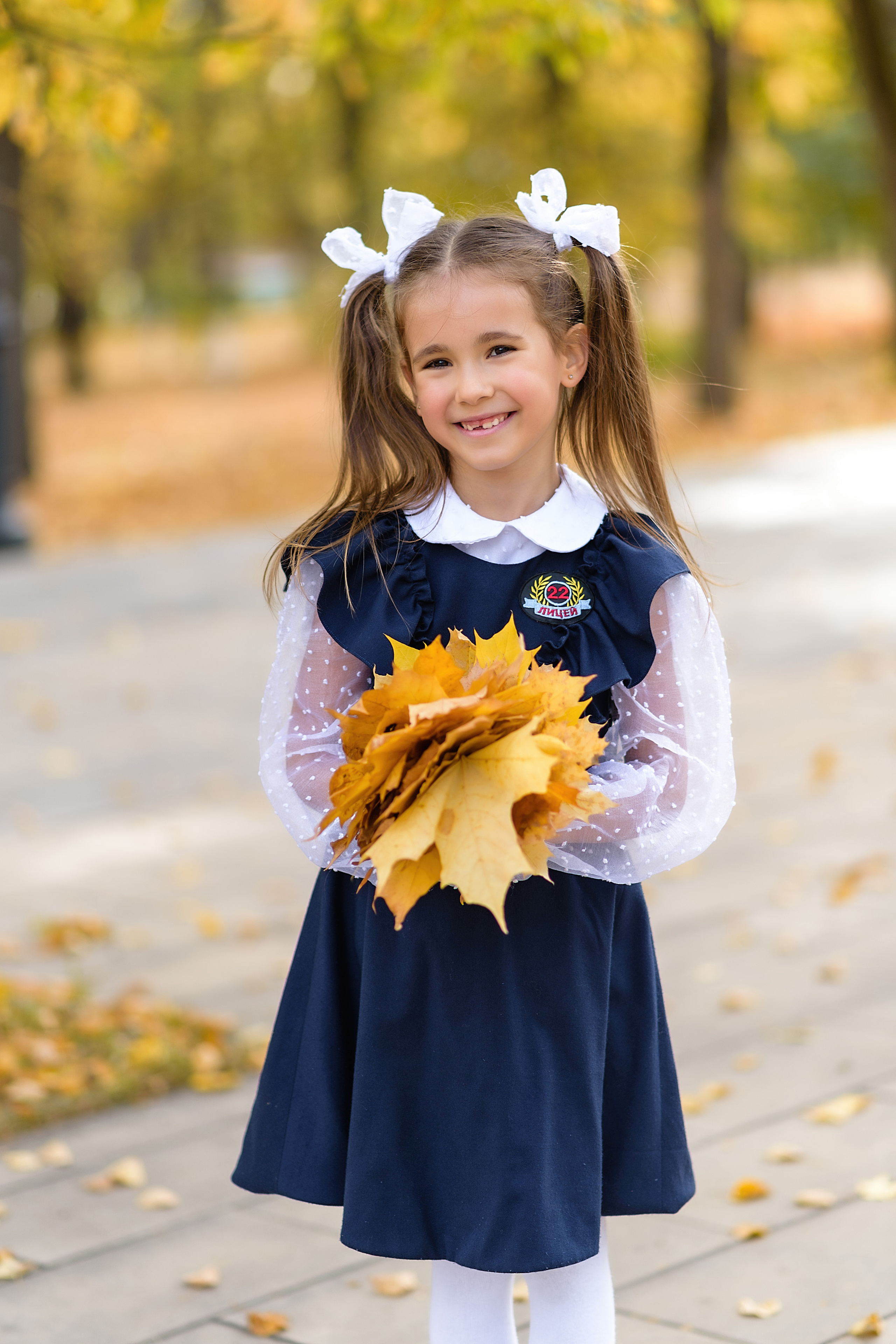 Портрет первоклассницы в школьной форме золотой осенью с букетом кленовых листов