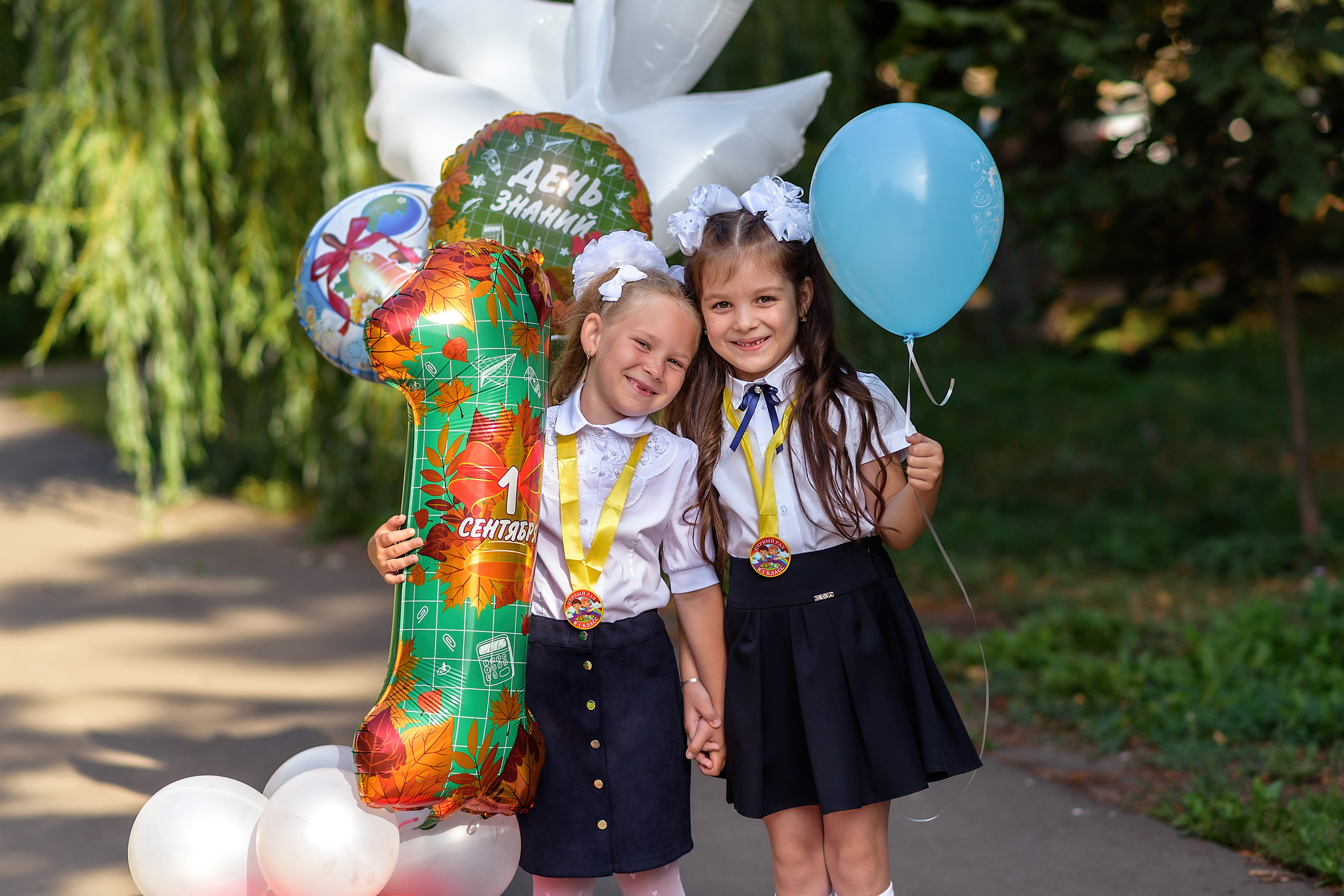 Две подружки в школьной форме фотографируются на празднике с шариками