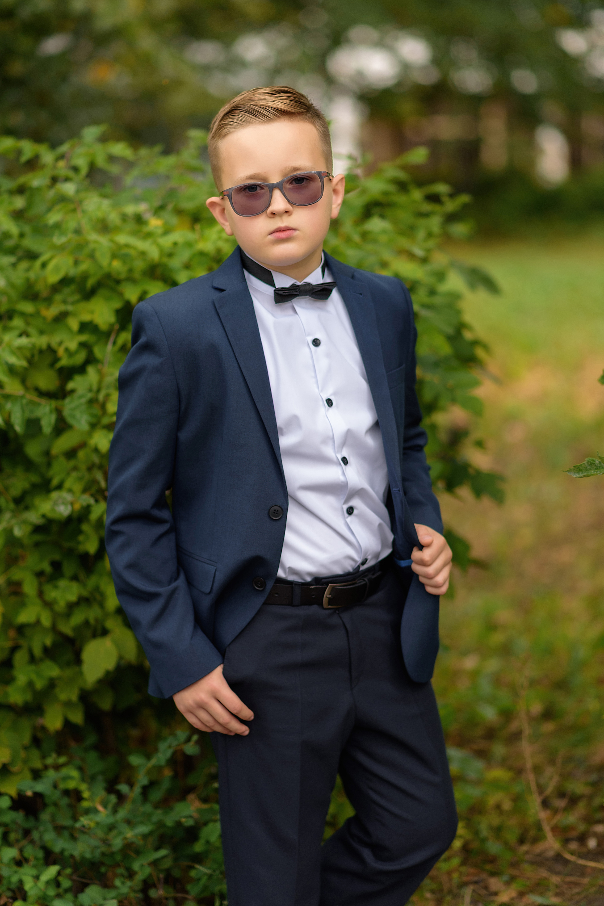 Портрет выпускника 4 класса в школьной форме с бабочкой и в очках на школьном дворе