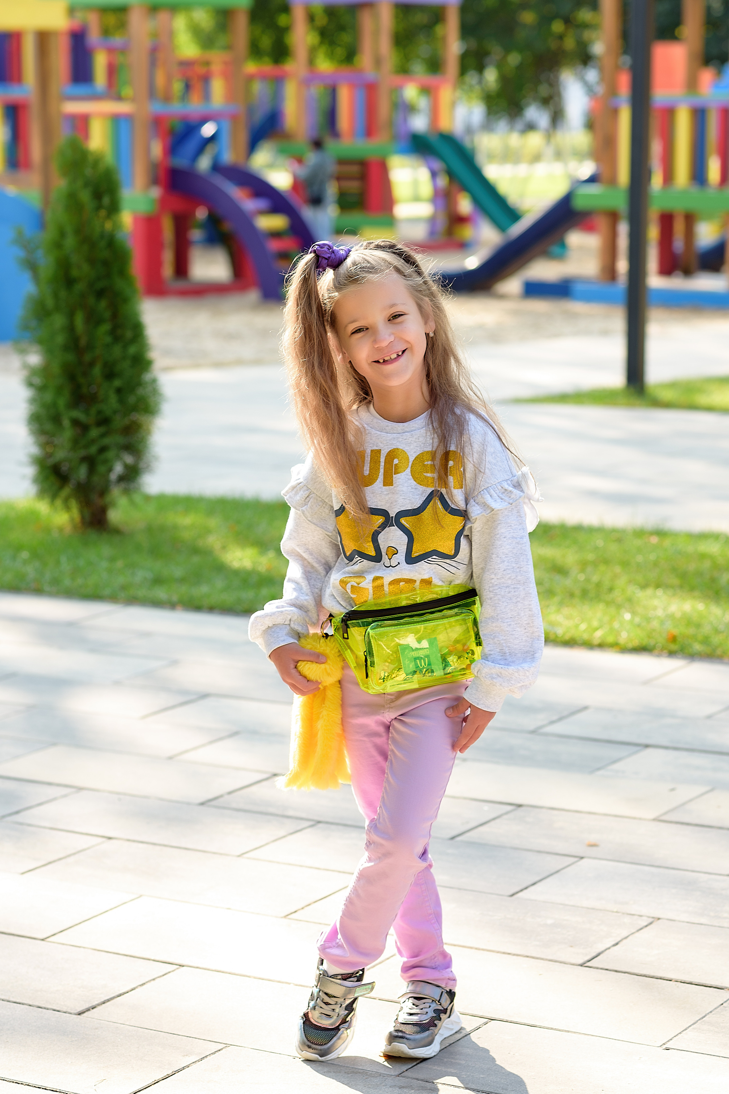 Девочка стоит на площадке в городском парке и улыбается