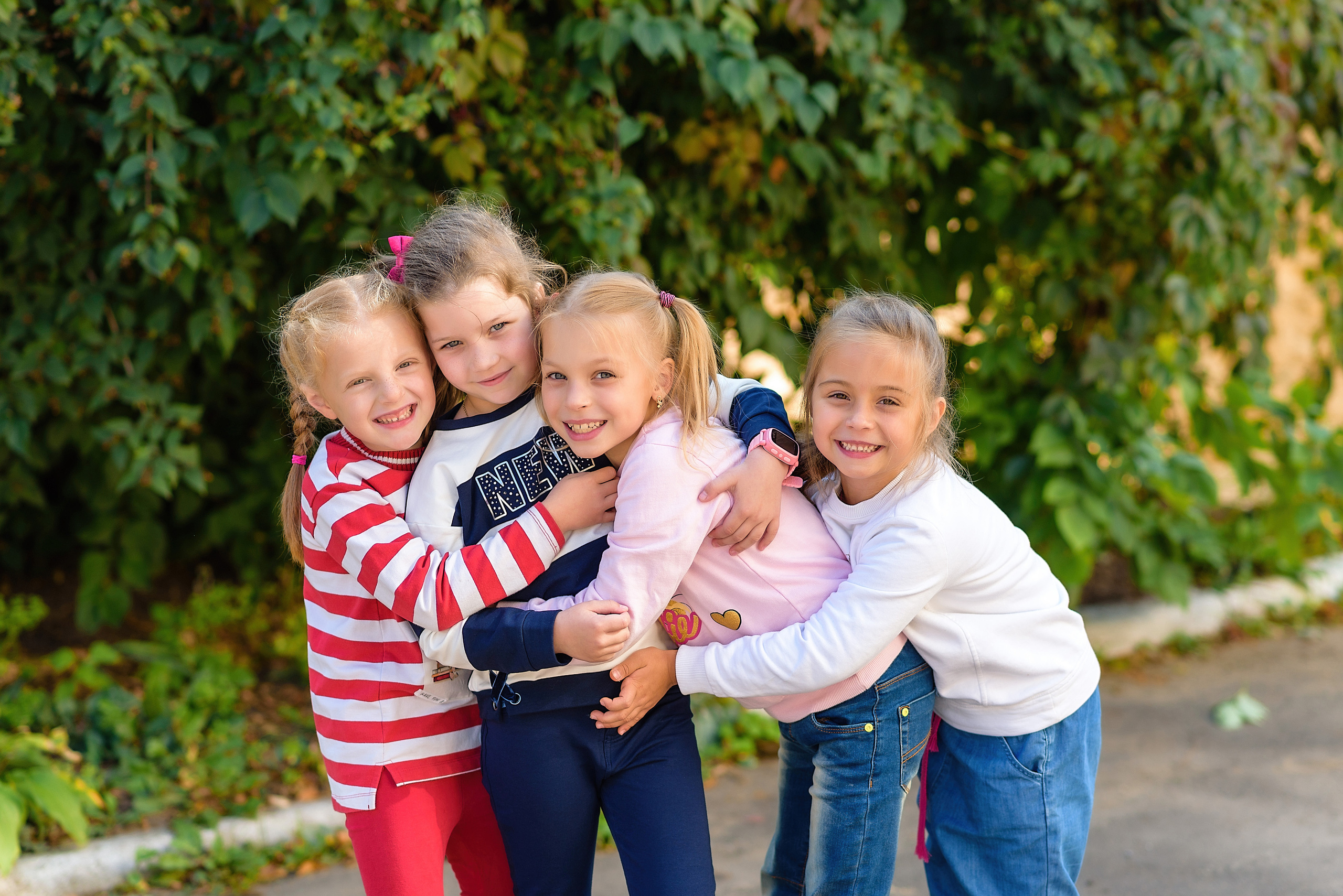 Четыре подружки из детского сада крепко обнимаются и смеются на детской площадке