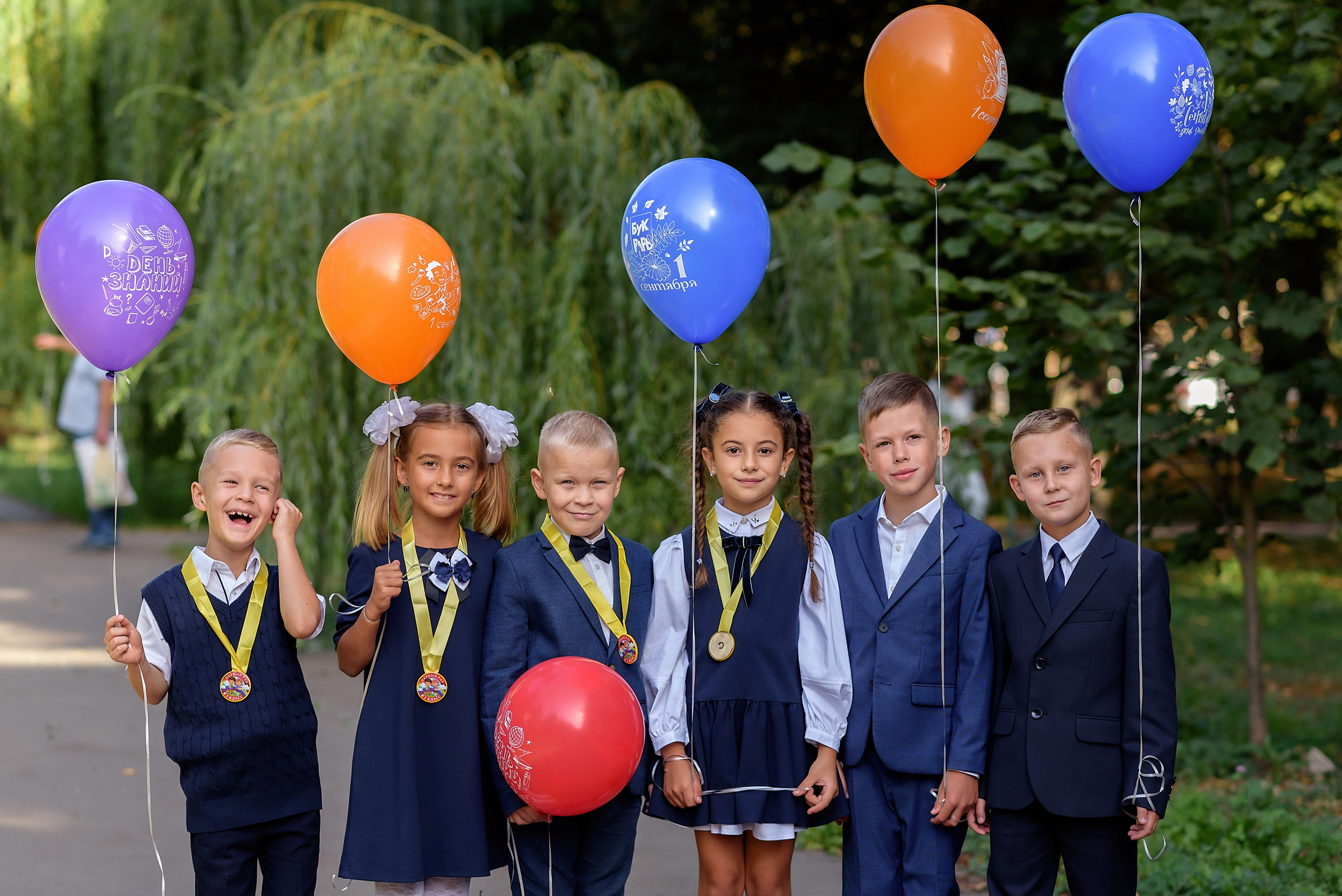 Групповая фотография на первое сентября с шариками в сквере, ученики первого класса в школьной форме