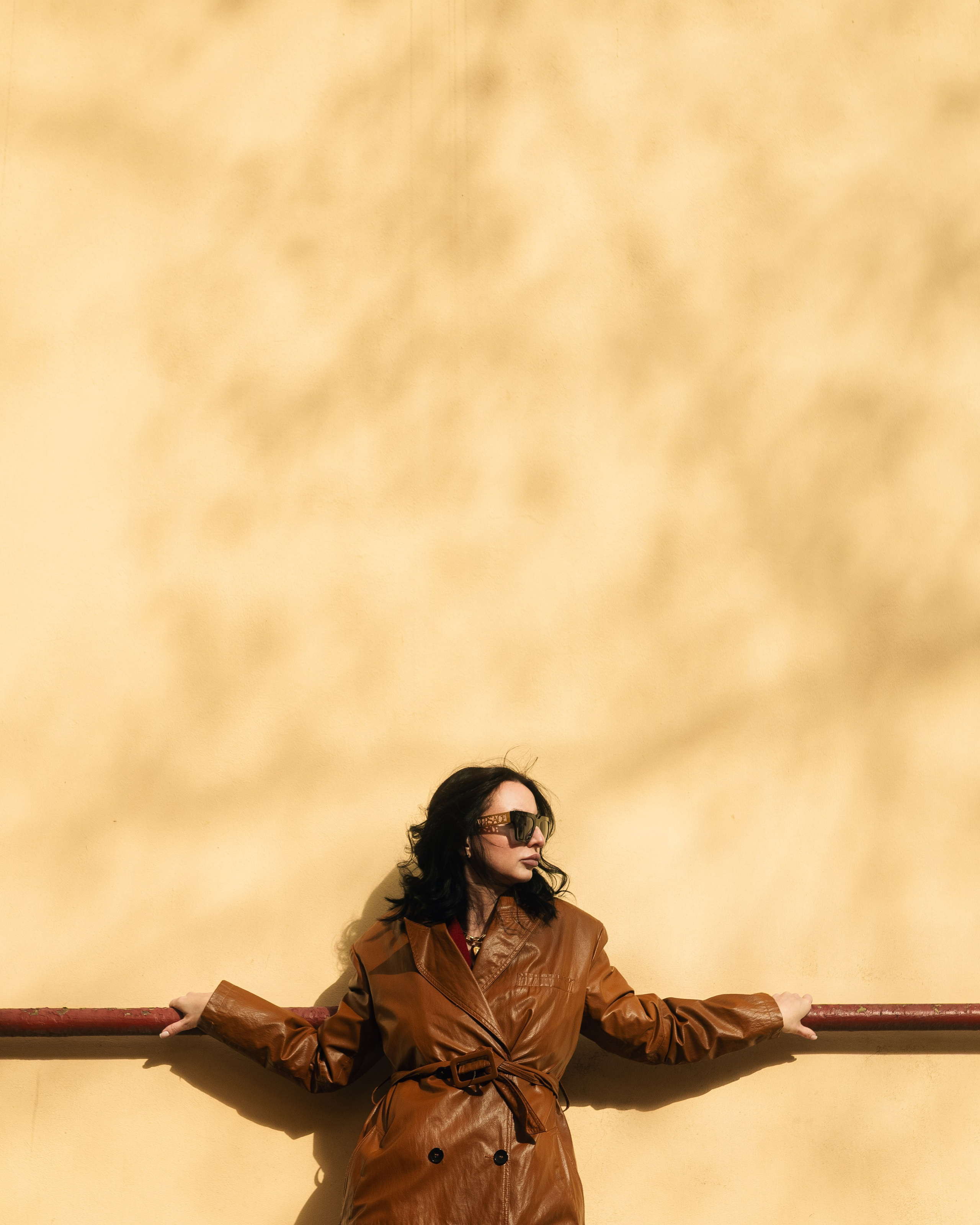 девушка в коричневом пальто позирует на фоне стены доходного дома с жёстким светом