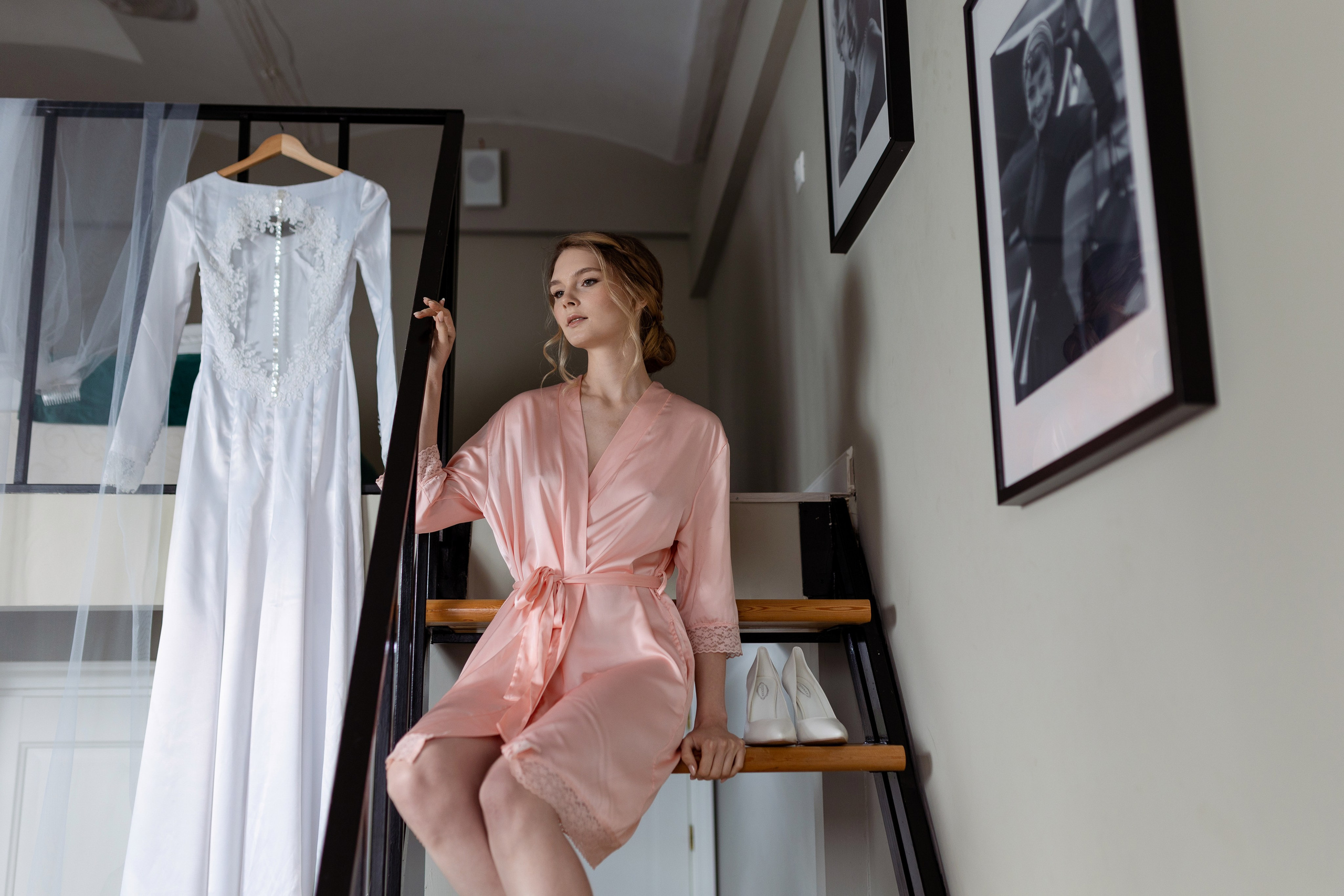 Невеста сидит на лестнице на фоне белоснежного платья.