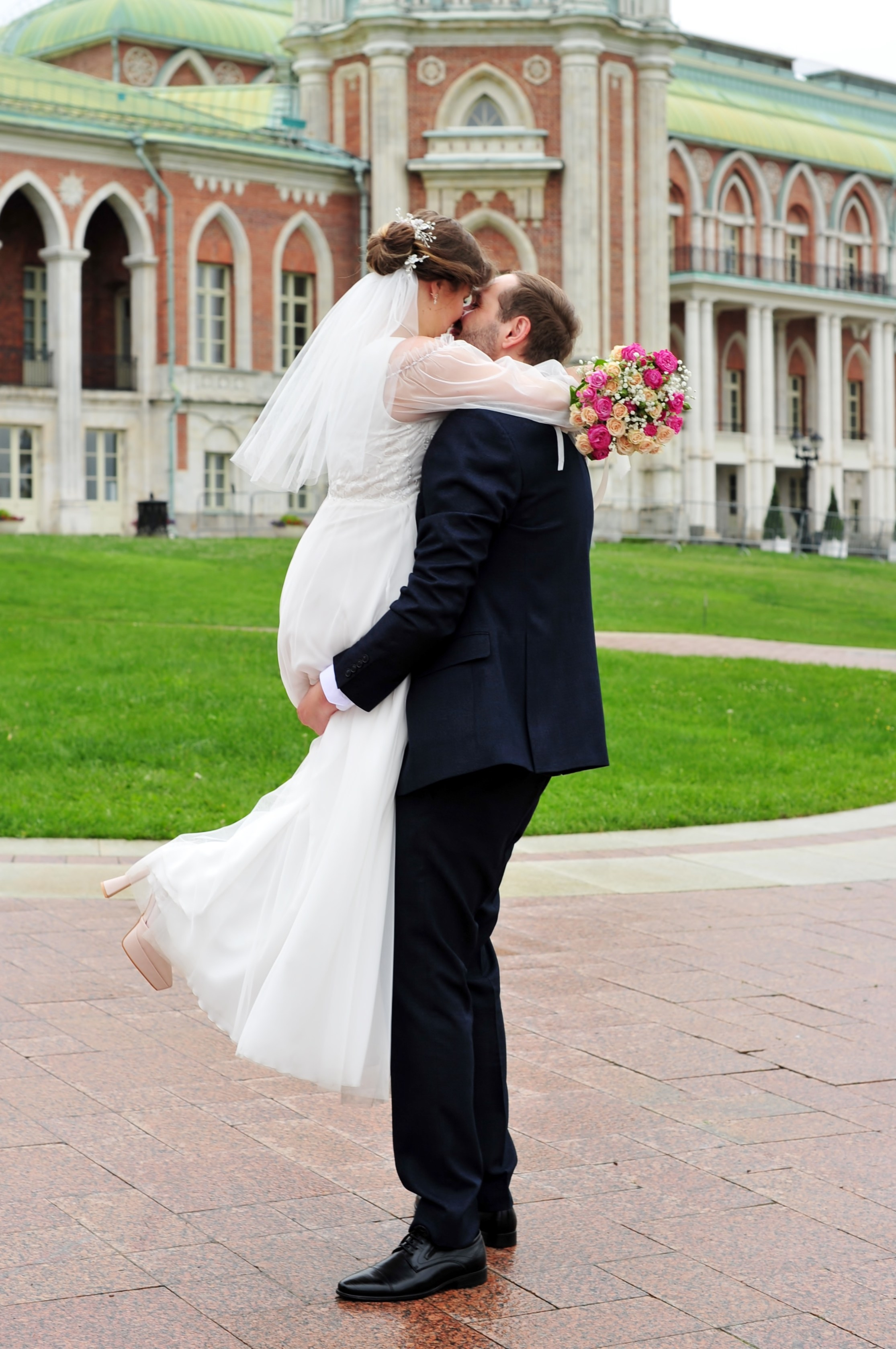 Свадьба в Царицыно пасмурным летним днем, жених приподнял невесту нод землей  