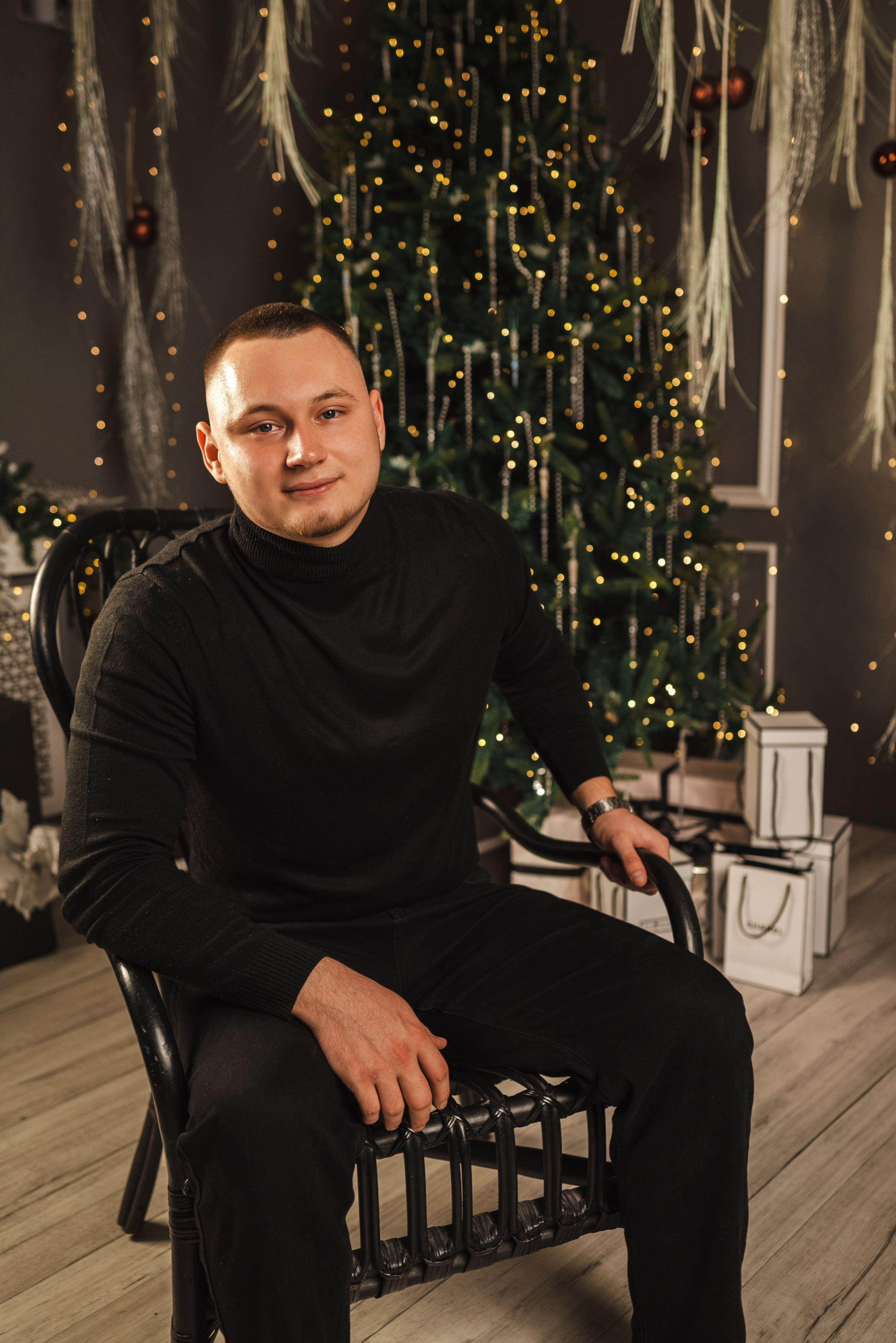 Новогодняя фотосессия 2025 в фотостудии в Каменске-Шахтинском и Ростове-на-Дону. Мужчина парень сидит в кресле на фоне новогодней елки. Фотограф Ольга Сагал 