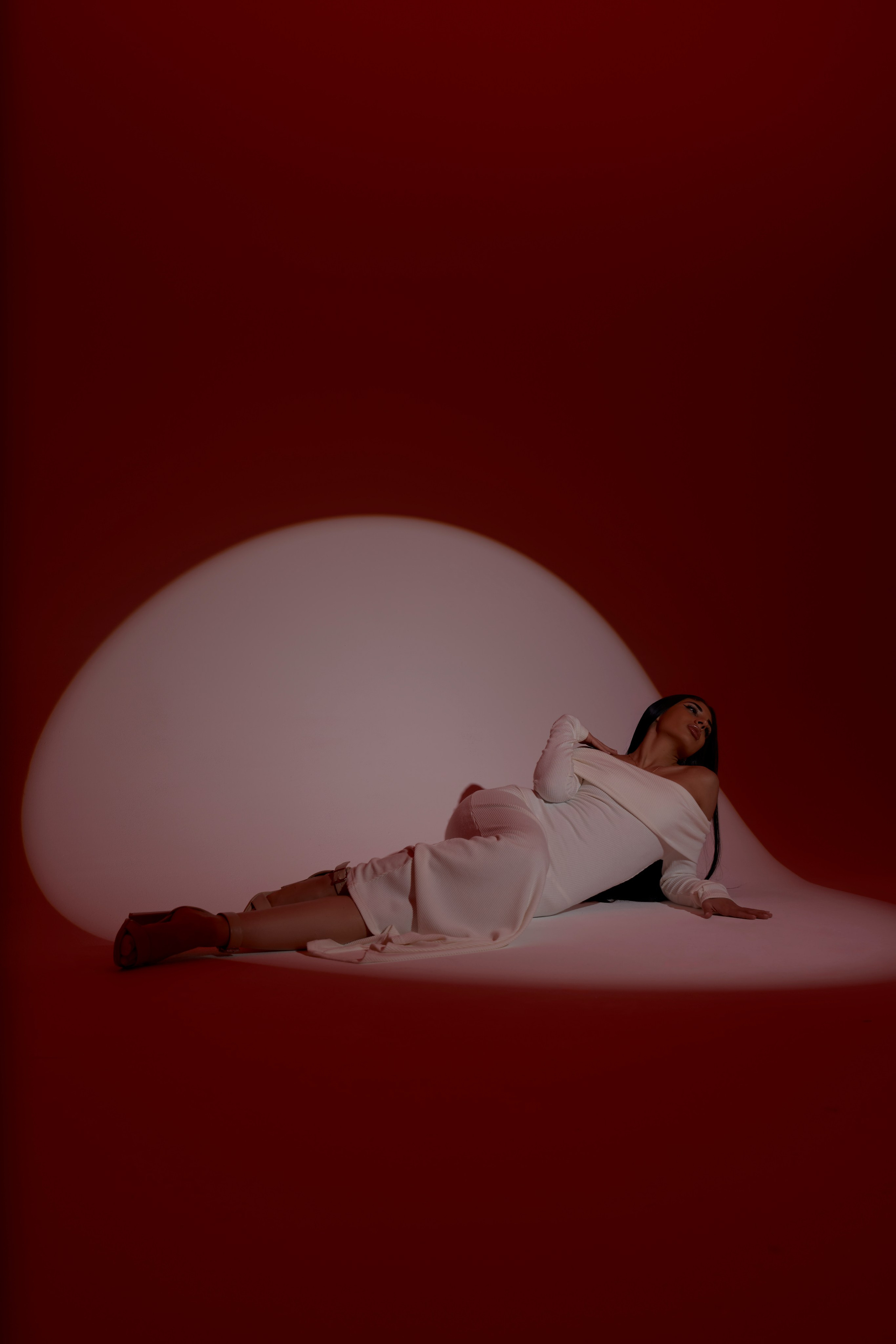 Fashion-фотосессия в Москве: девушка в белом лежит на фоне красной стены с кругом света, графичная композиция
