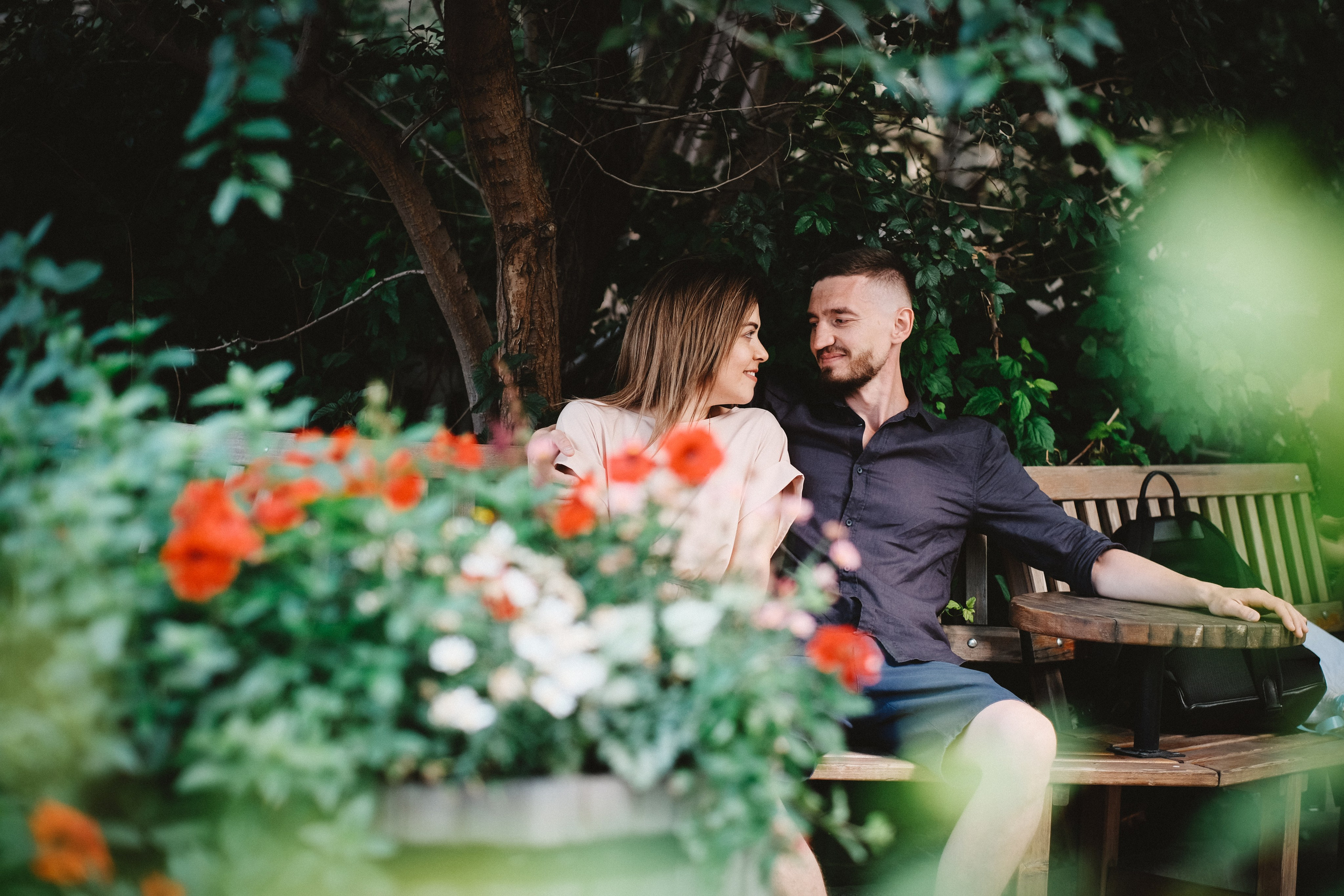 Влюбленные сидят на скамейке. На переднем плане цветы. Съёмка сквозь цветы.