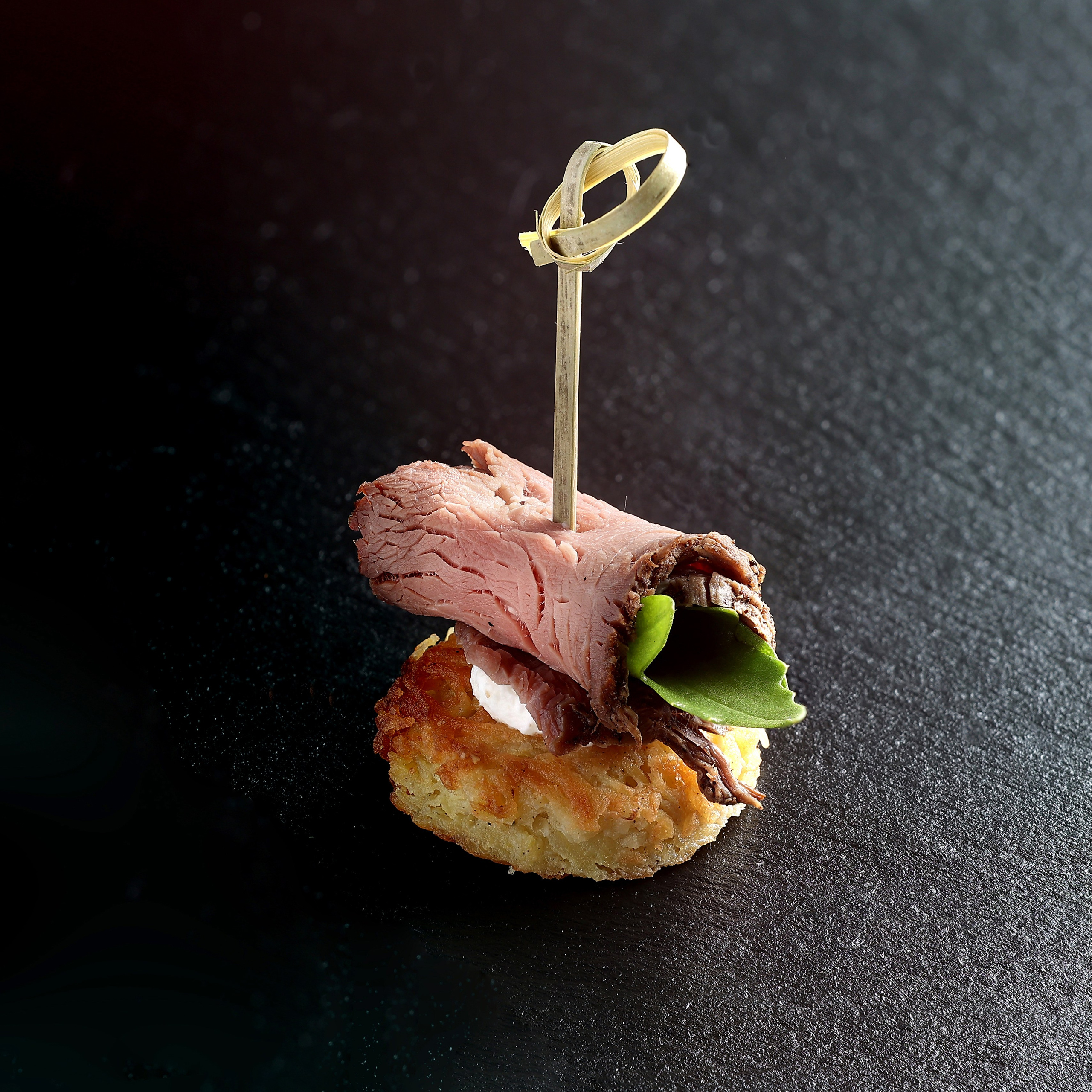 Мини-драник с крем-сыром и рулетом из ростбифа с петрушкой, собранные шпажкой.