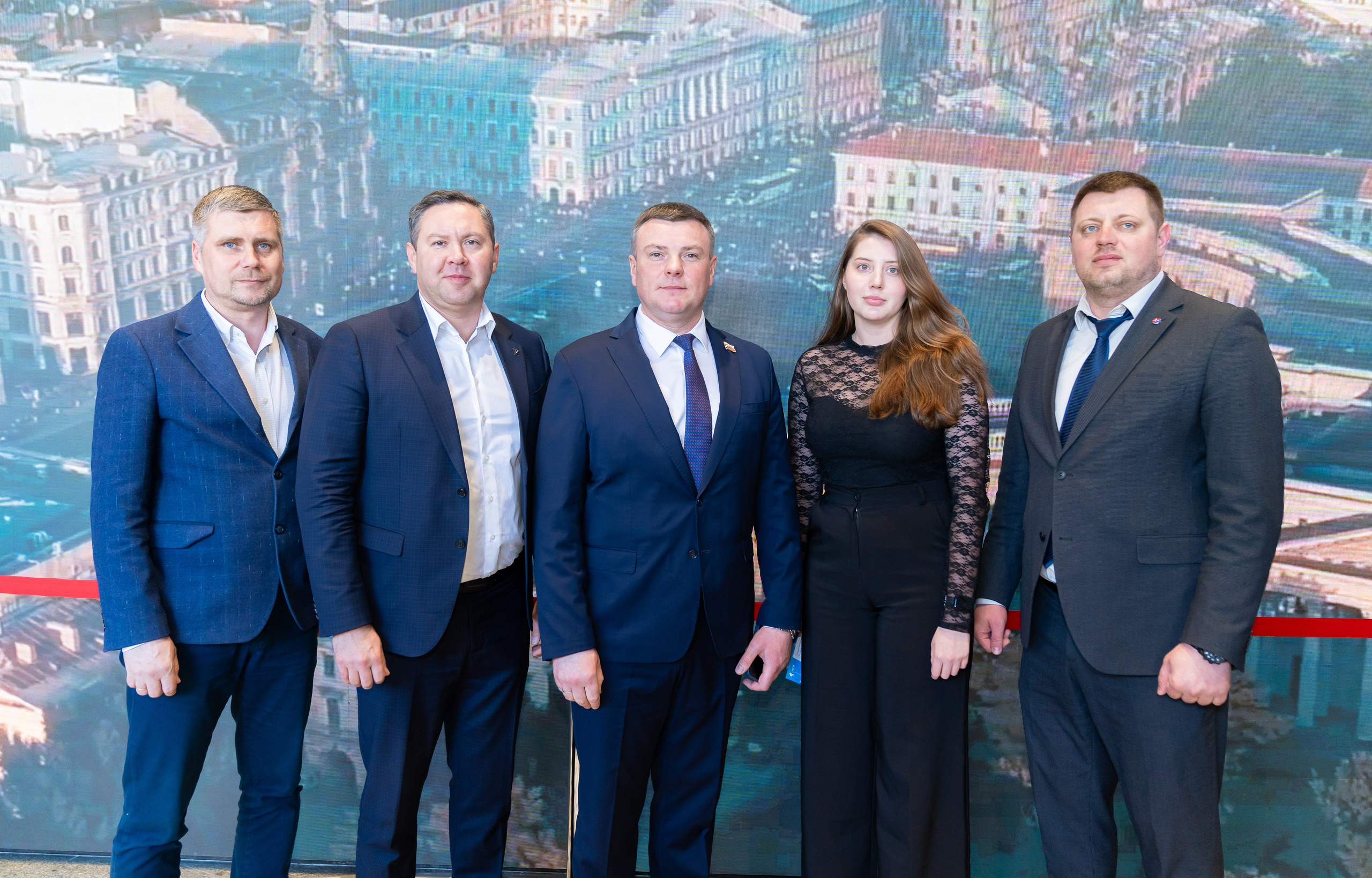Официальная группа на Дне местного самоуправления в Санкт-Петербурге. Четыре мужчины и одна женщина в деловых костюмах на фоне городской панорамы. Фото Евгения Мальцева.