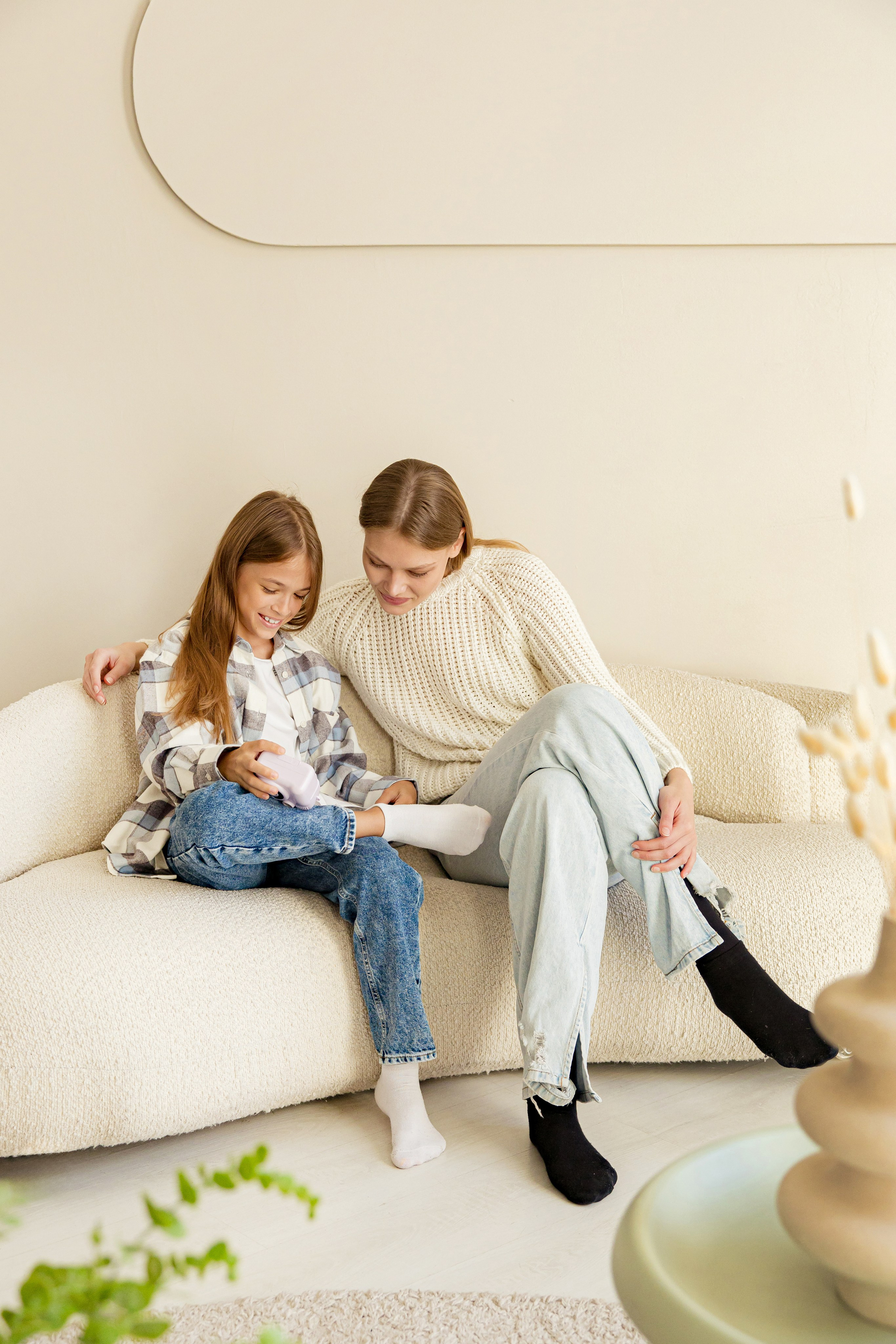 Две девушки сидят на диване в фотостудии и рекламируют камеру моментальной печати