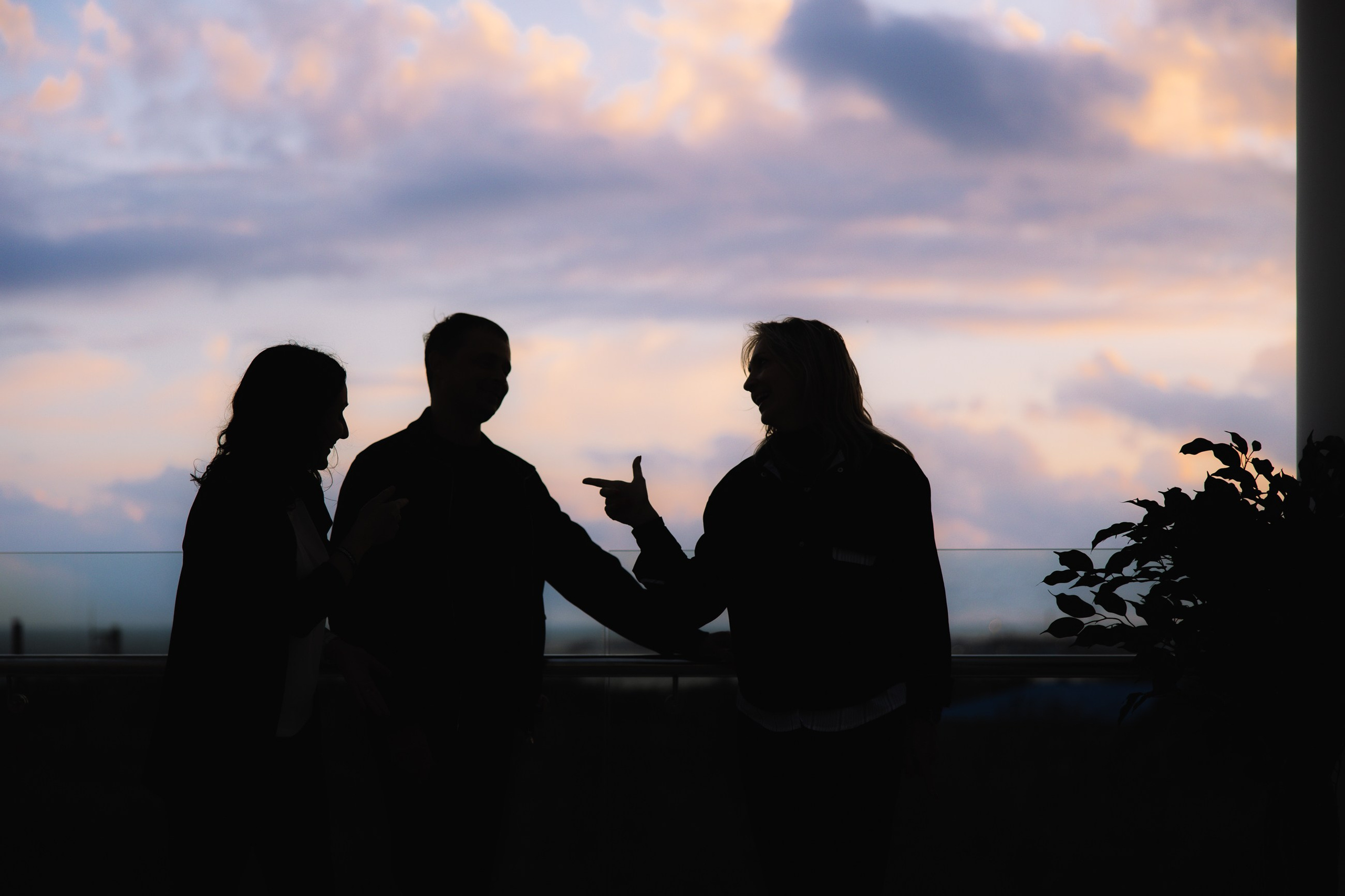 Силуэты на закате: Три участника общаются на фоне вечернего неба, завершающий атмосферный кадр бизнес-дня.