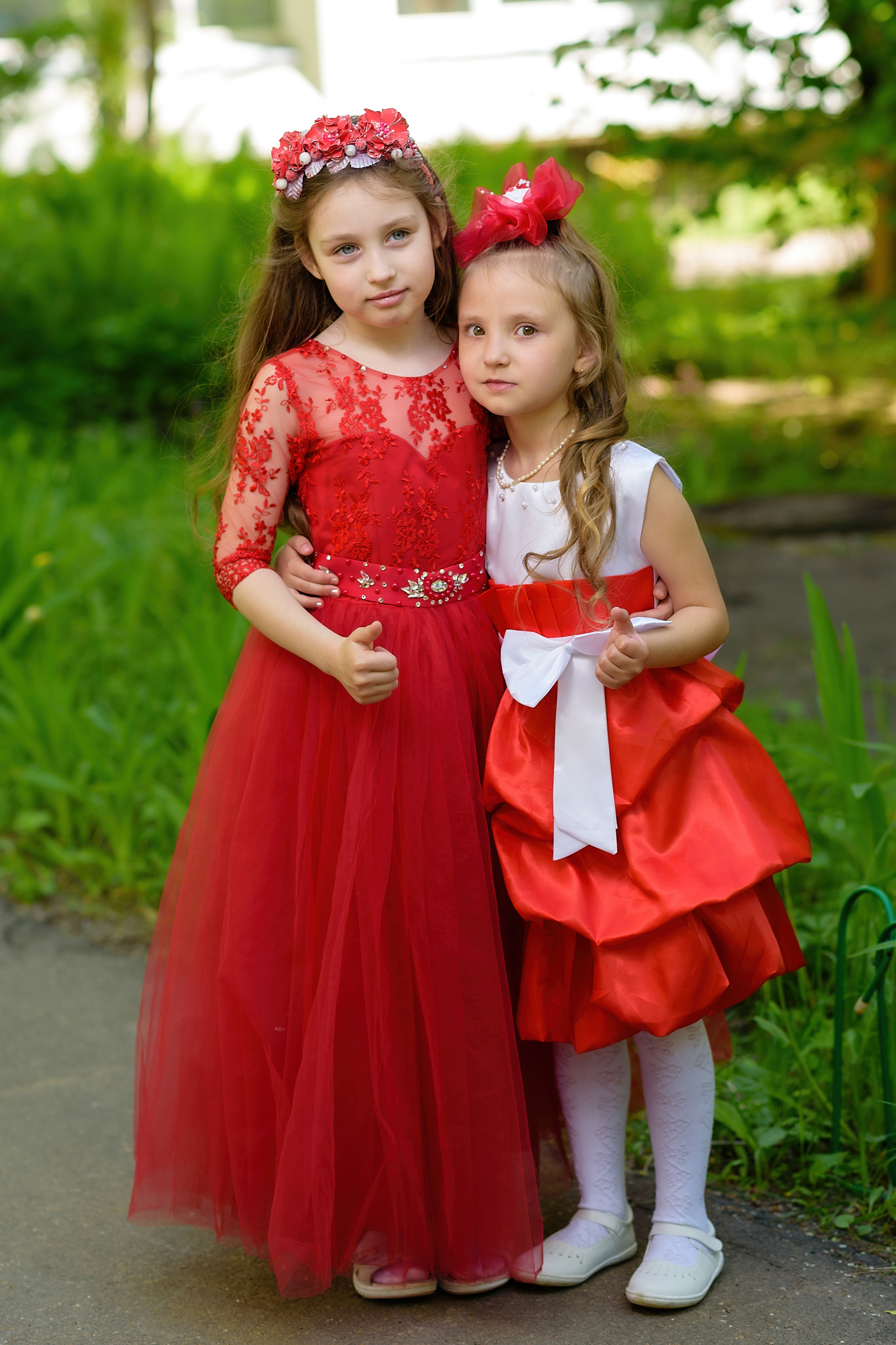 Выпускницы из детского сада стоят в праздничных платьях, обнявшись, на улице