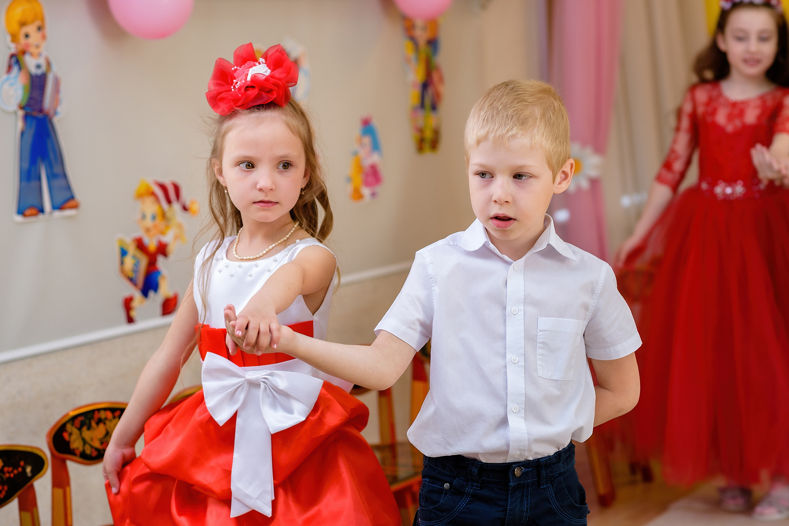 Девочка и мальчик в праздничной одежде танцуют на выпускном из детского сада