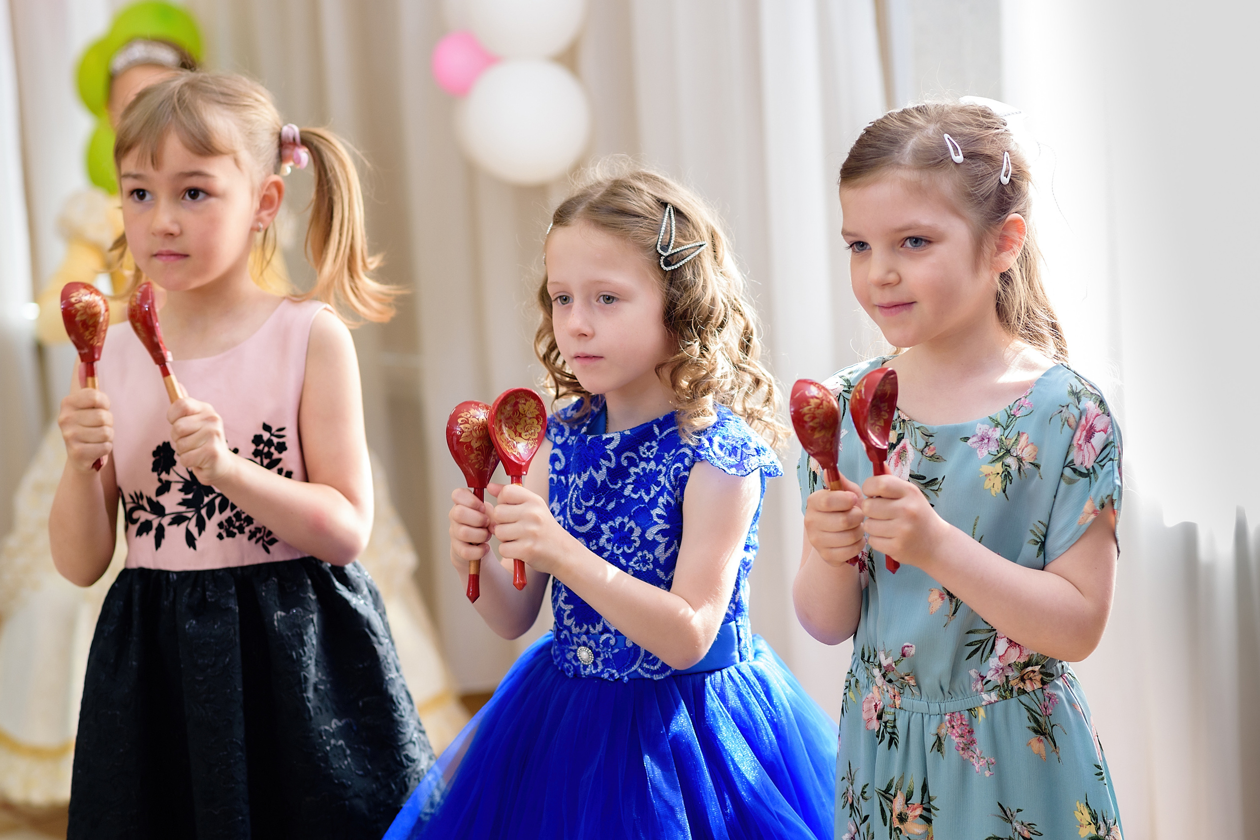 Три девочки играют на деревянных ложках на выпускном из детского сада