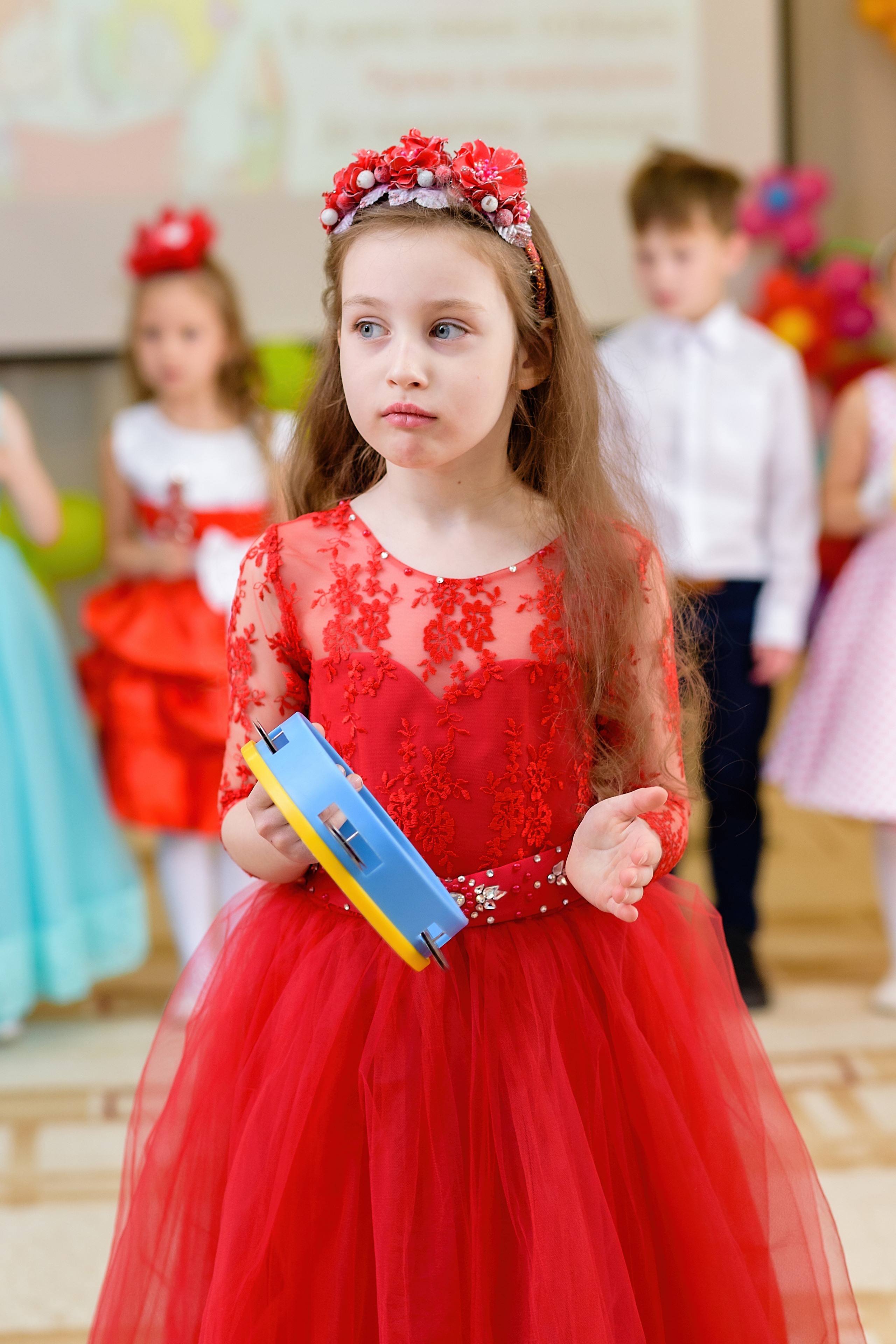 Девочка в красном платье играет на бубне на выпускном из детского сада