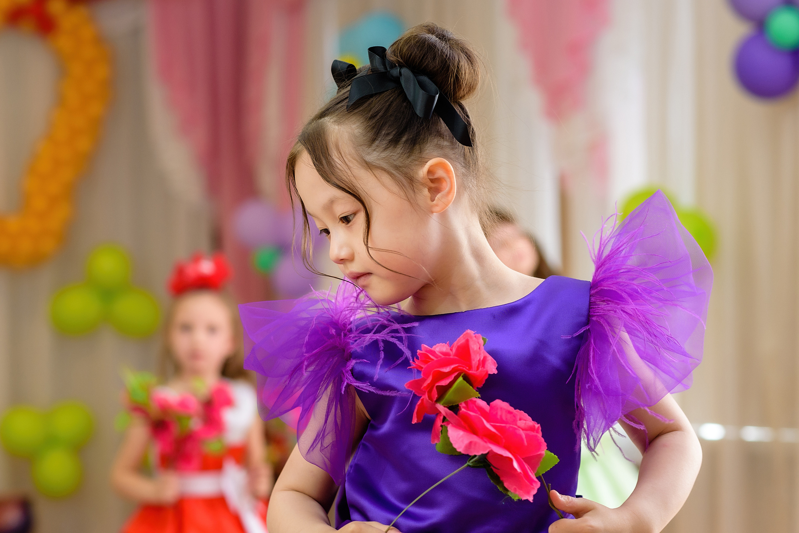 Девочка в фиолетовом платье танцует с цветами на выпускном из детского сада