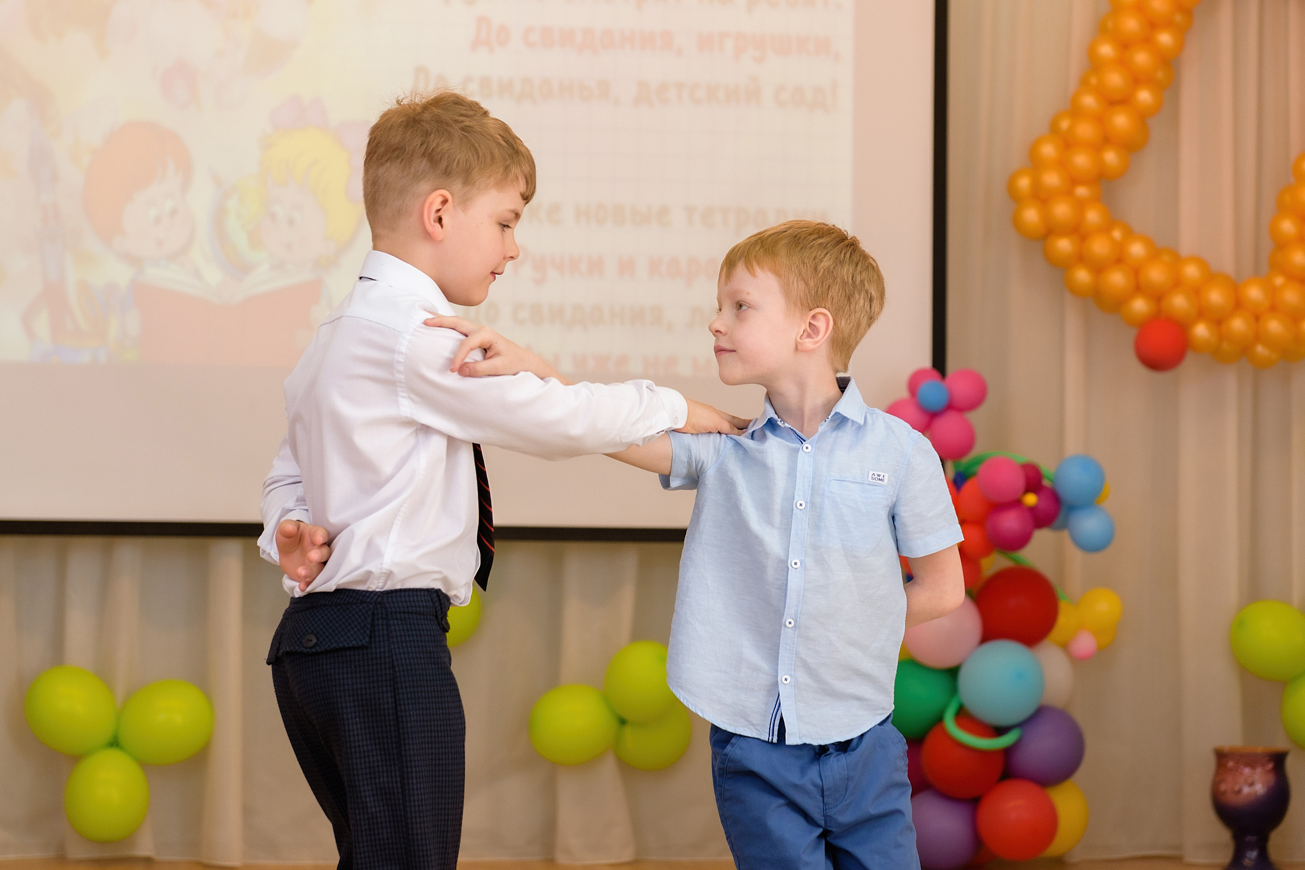 Два выпускника танцуют в музыкальном зале на утреннике