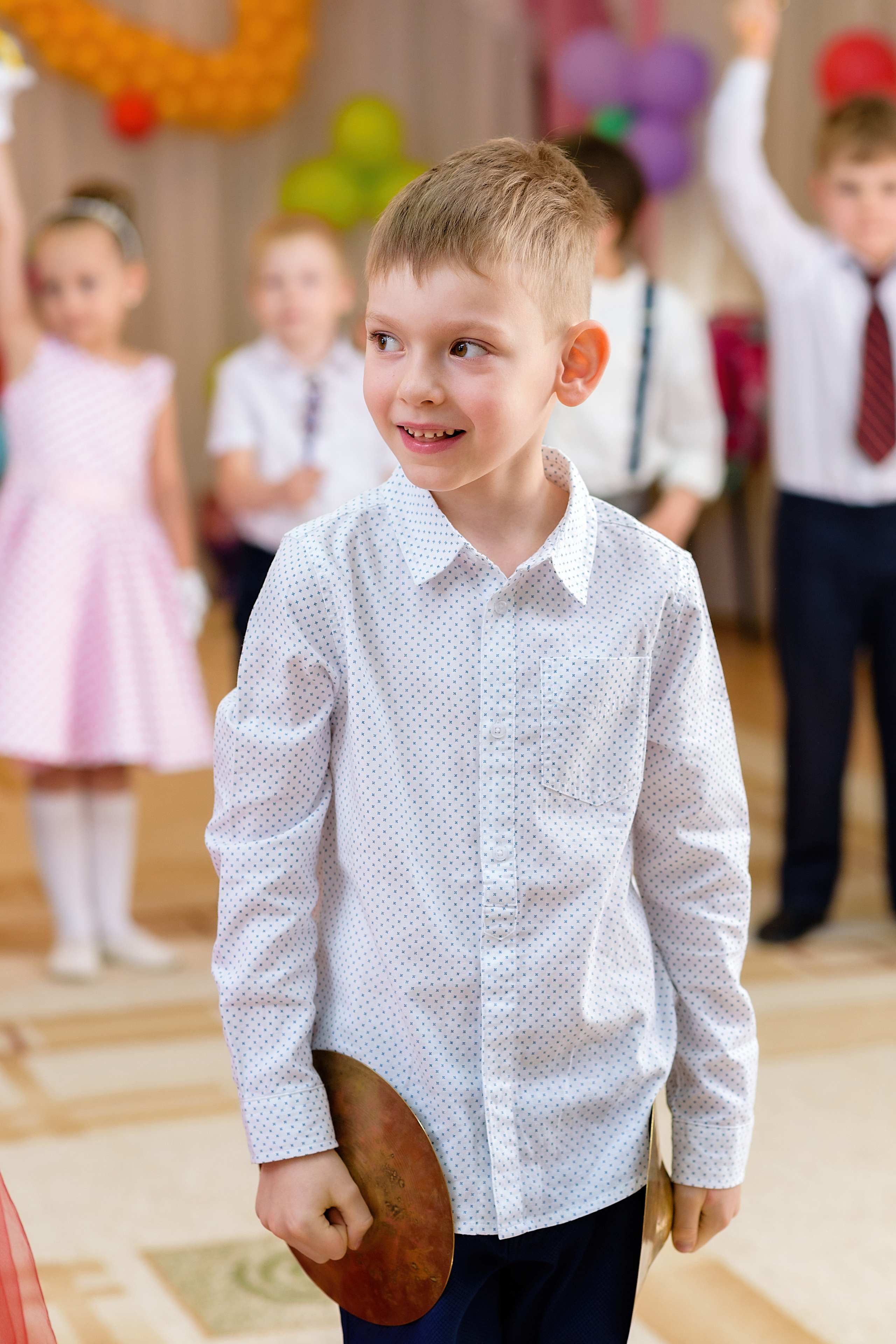 На выпускном утреннике мальчик стоит с музыкальными тарелками