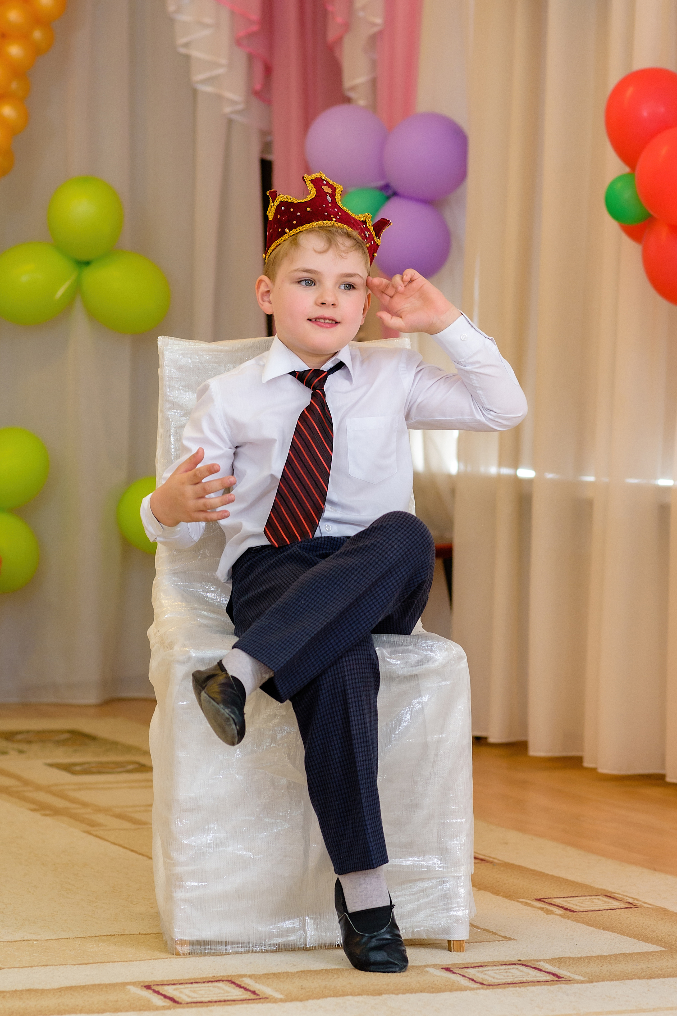 Мальчик на выпускном в детском саду играет короля. Он сел на вымышленный трон
