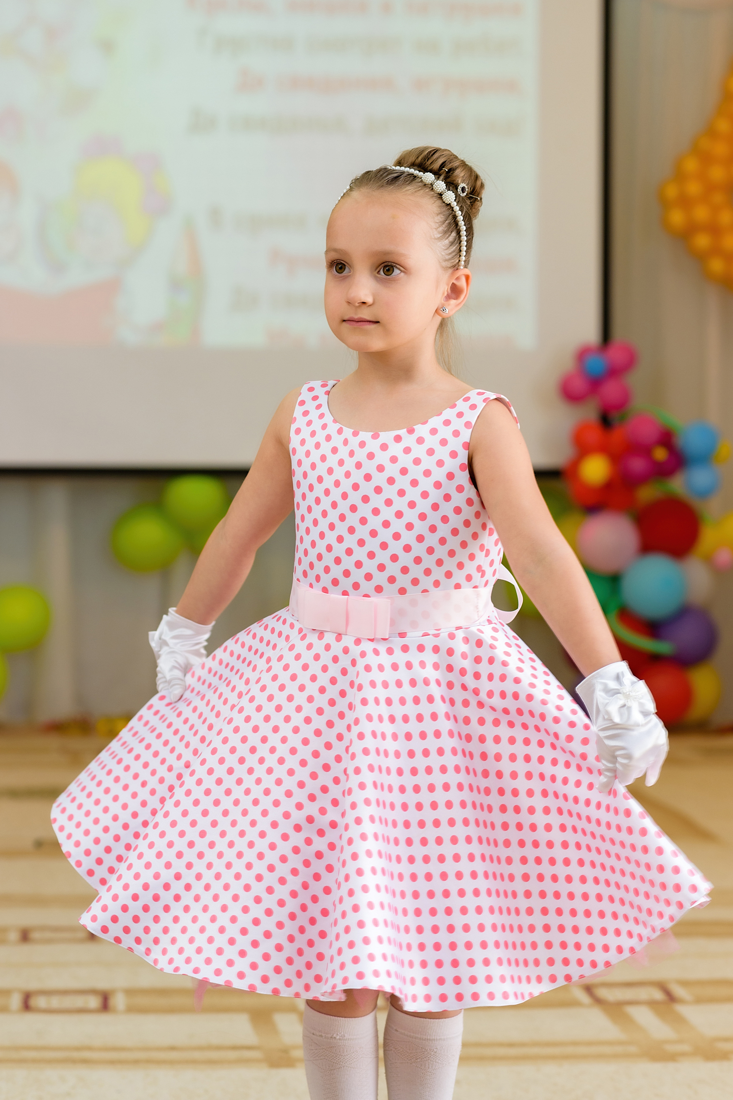 Девочка в праздничном платье танцует на выпускном из детского сада