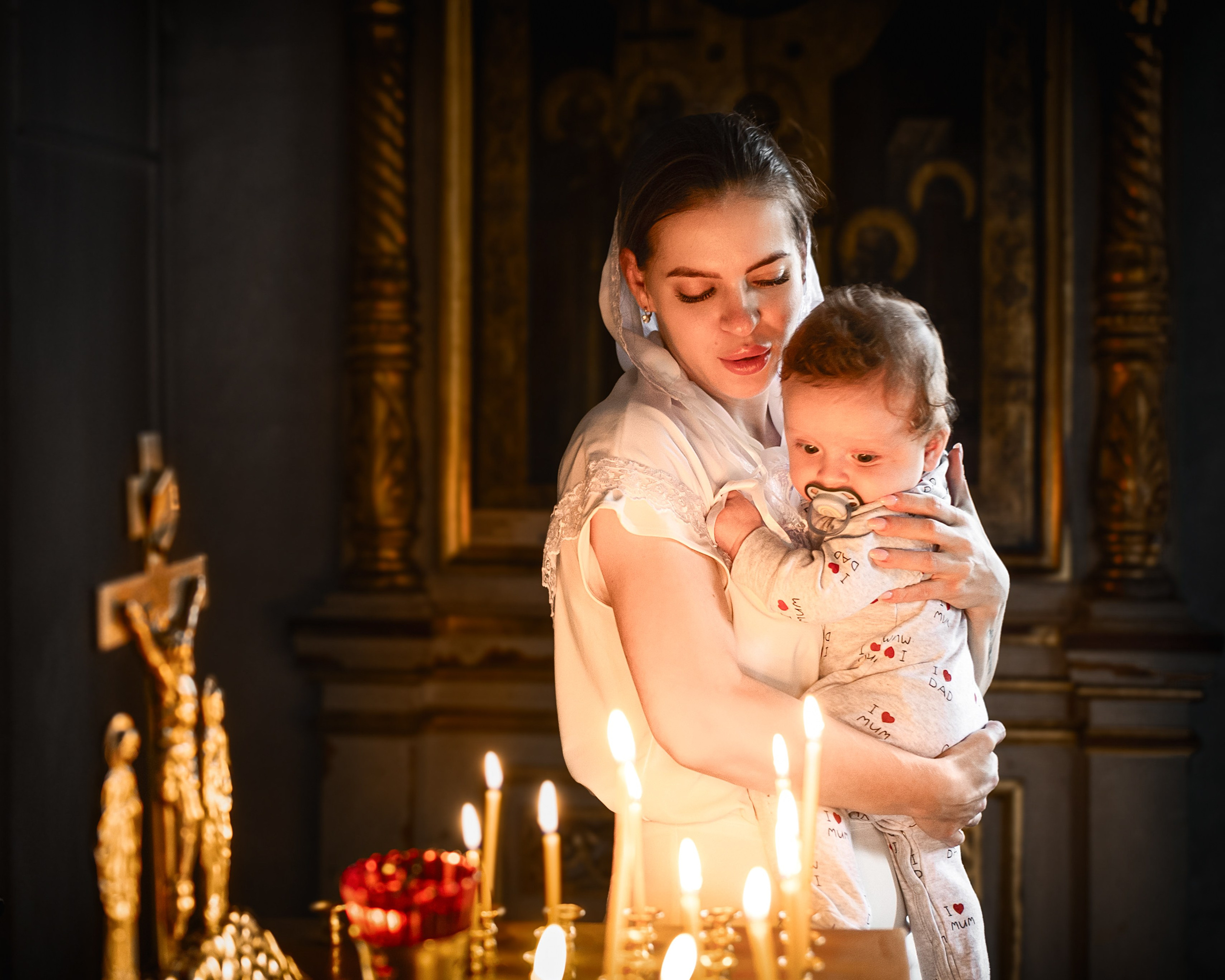 Мама с сыном на руках стоит возле свечек в храме