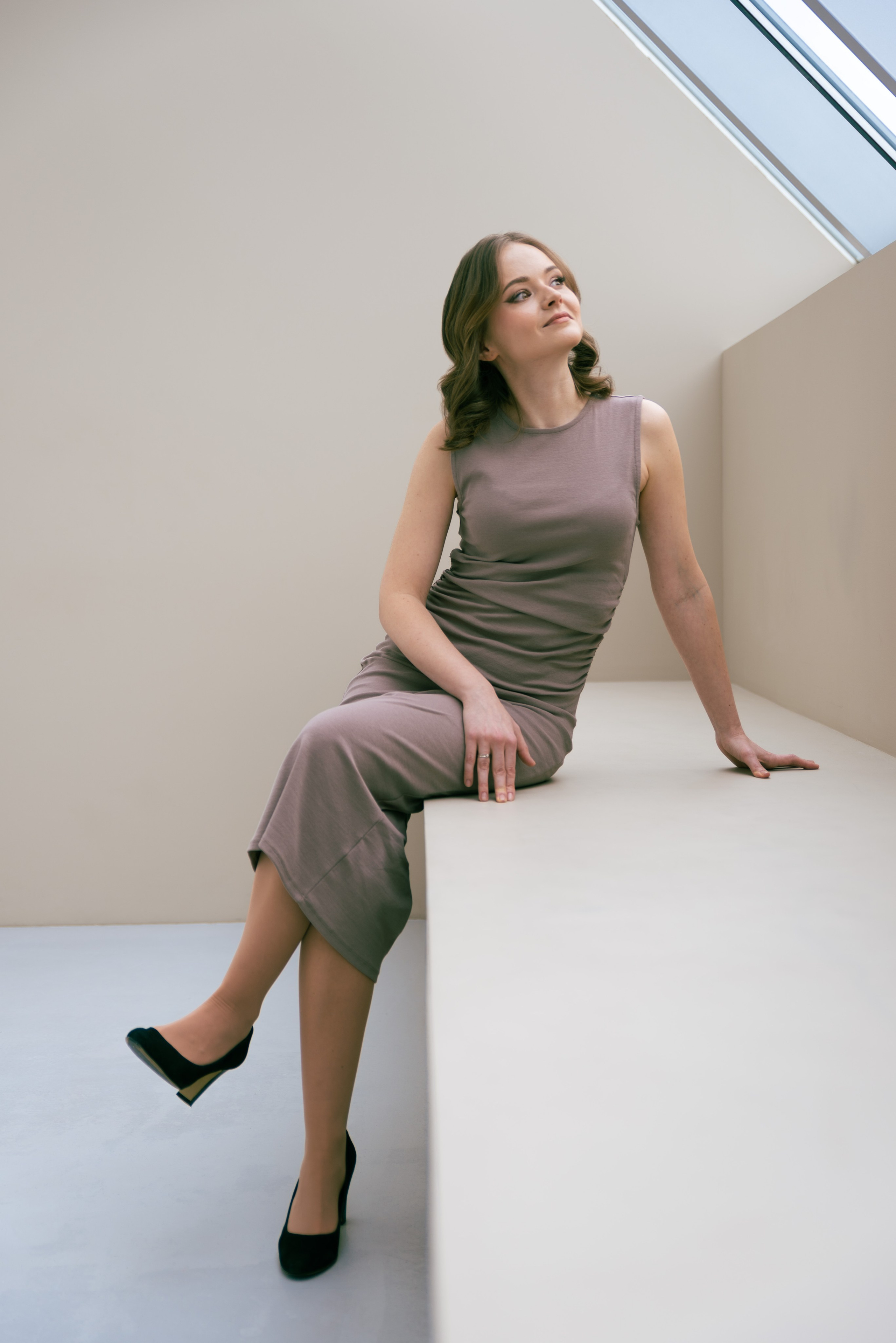 Интерьерная фотостудия естественный свет. Девушка в бежевом платье сидит у окна.