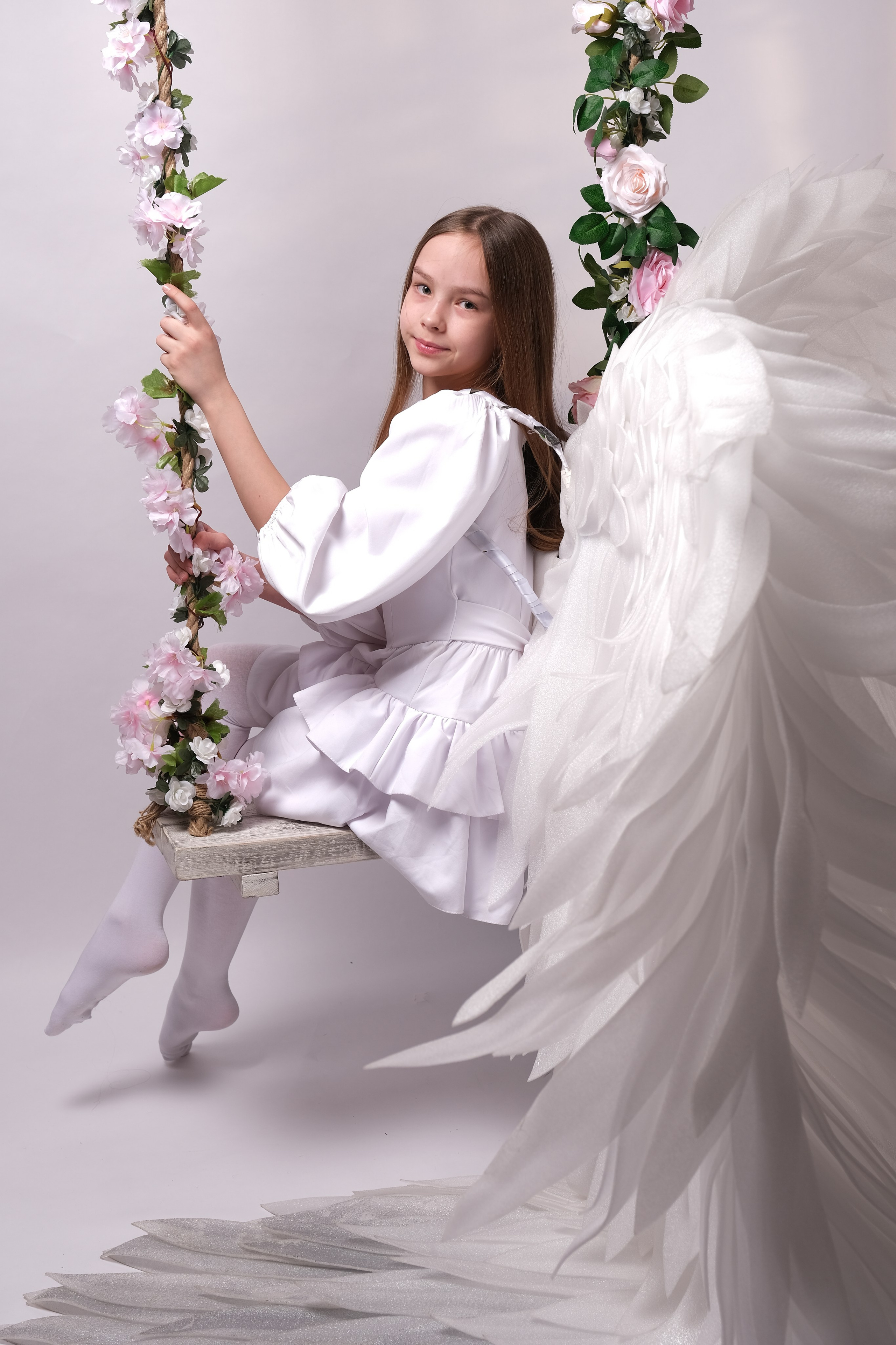 Юная девушка с крыльями ангела на качелях